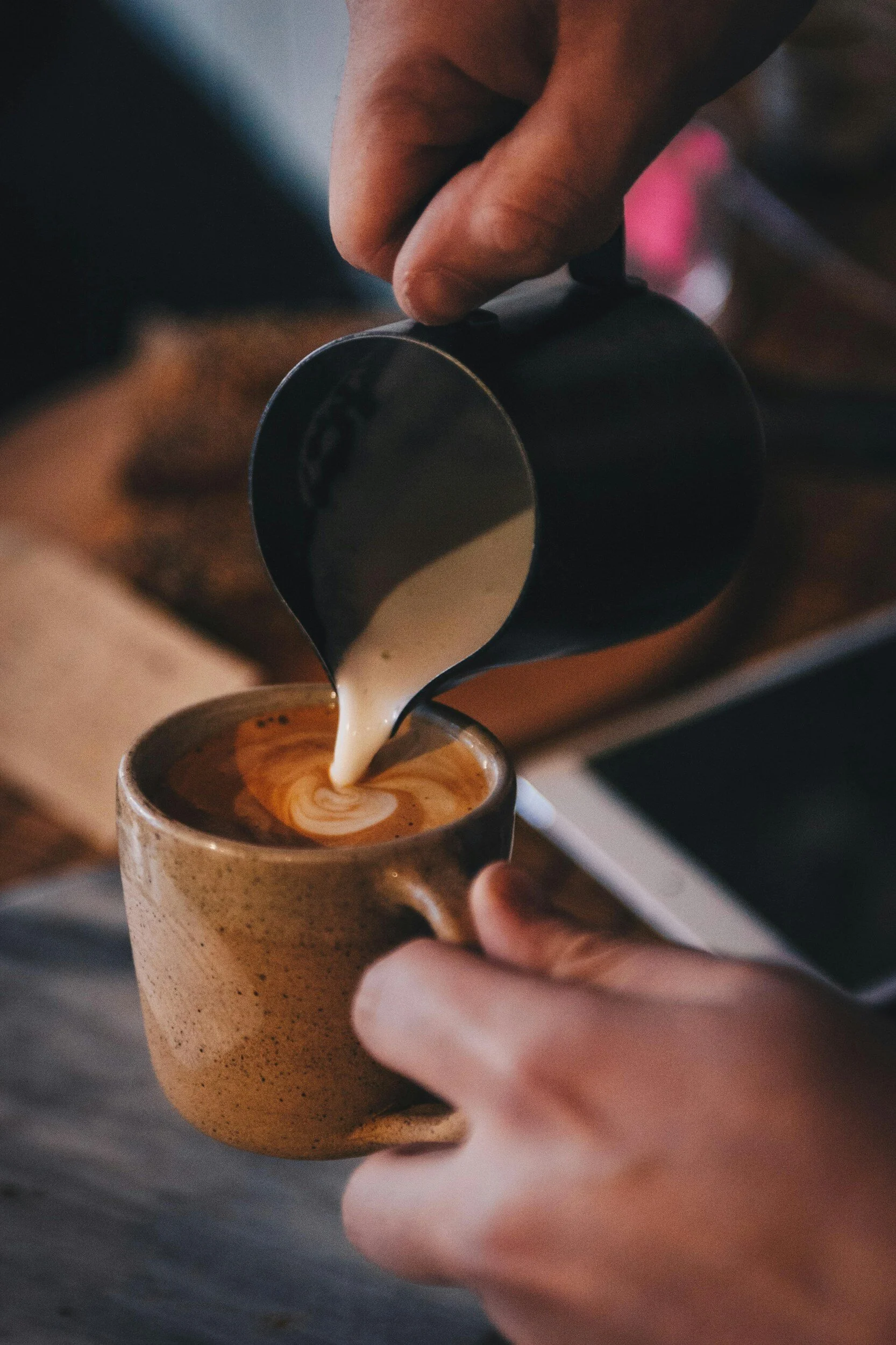 Person pouring steamed milk into a cup of coffee to make a latte art.