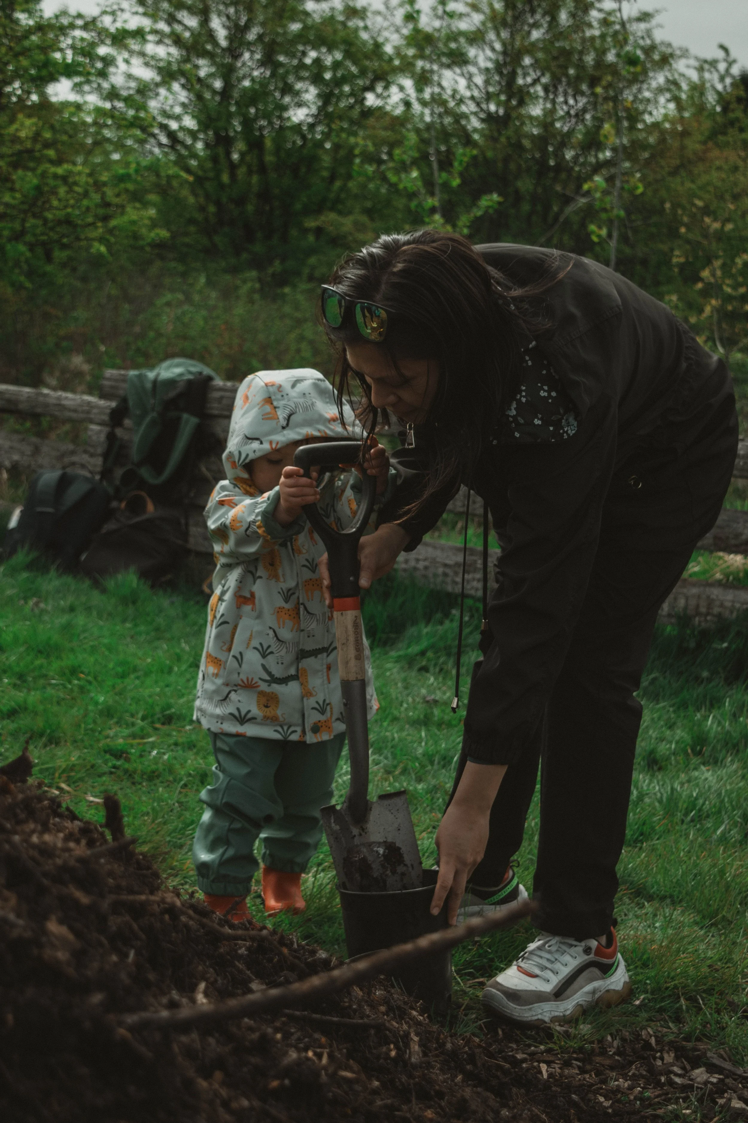 A woman and a young child planting a tree in an outdoor, forested area.