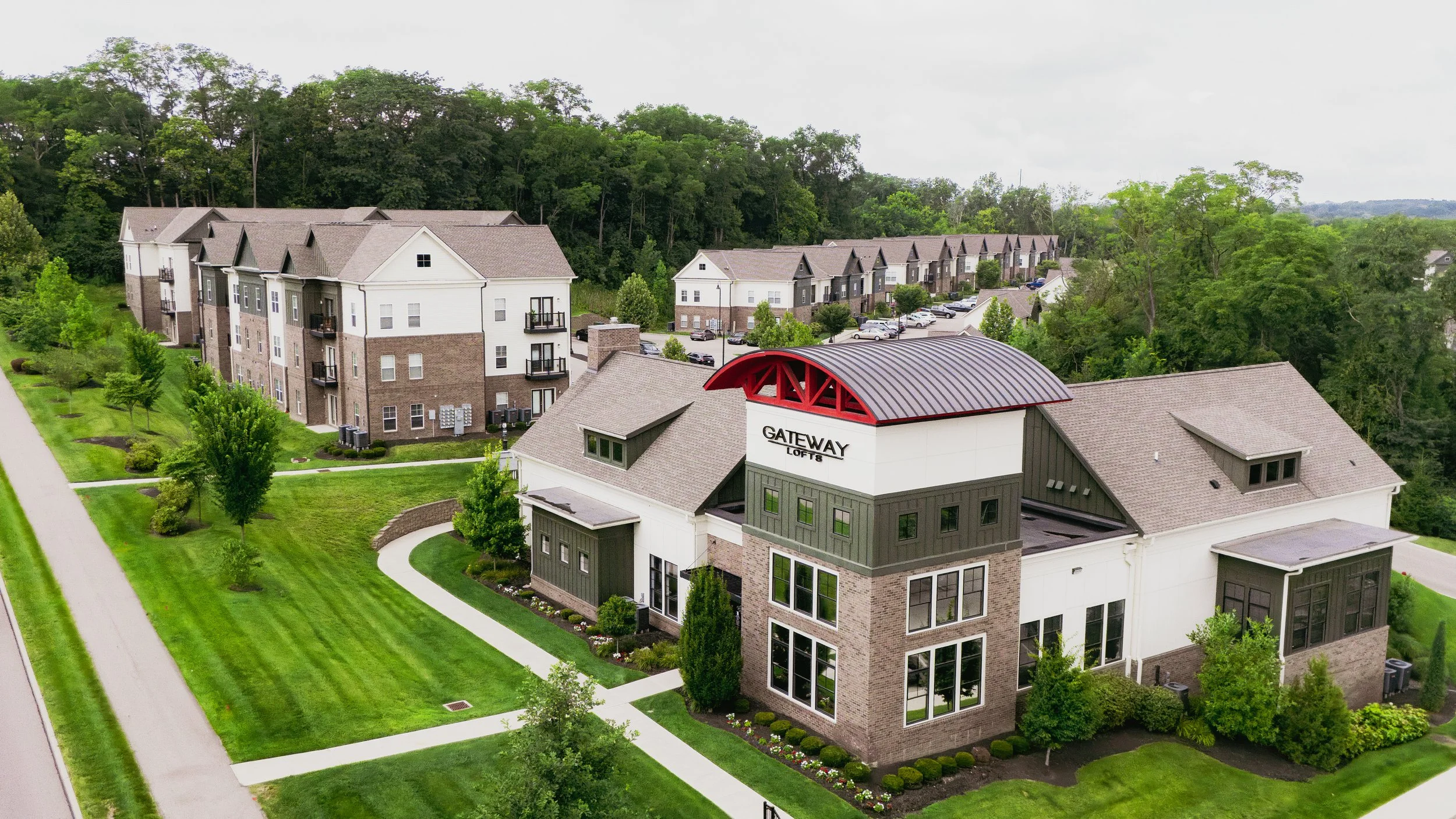 Aerial view of a residential apartment complex named 'Gateway Lofts' with green landscaped lawns, pathways, and multiple buildings surrounded by trees and parking lots.