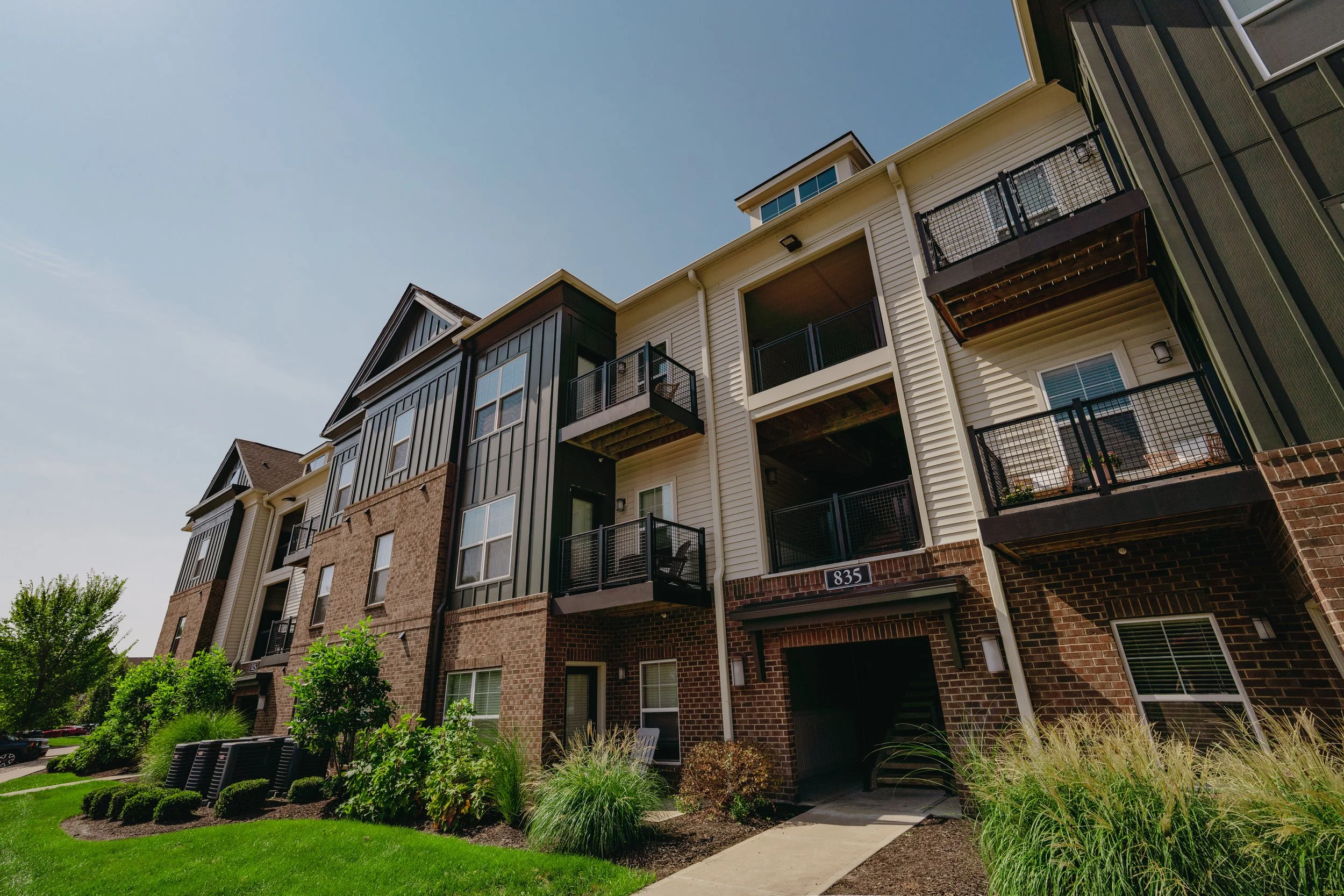 Multistory residential building with balconies, brick and siding exterior, and landscaped garden with pathways and seating.