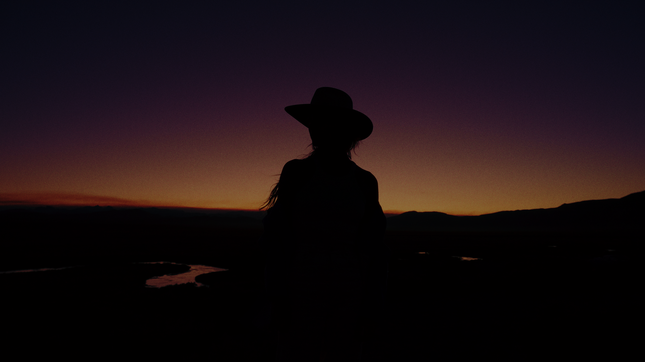 Silhouette of person wearing a hat against a sunset