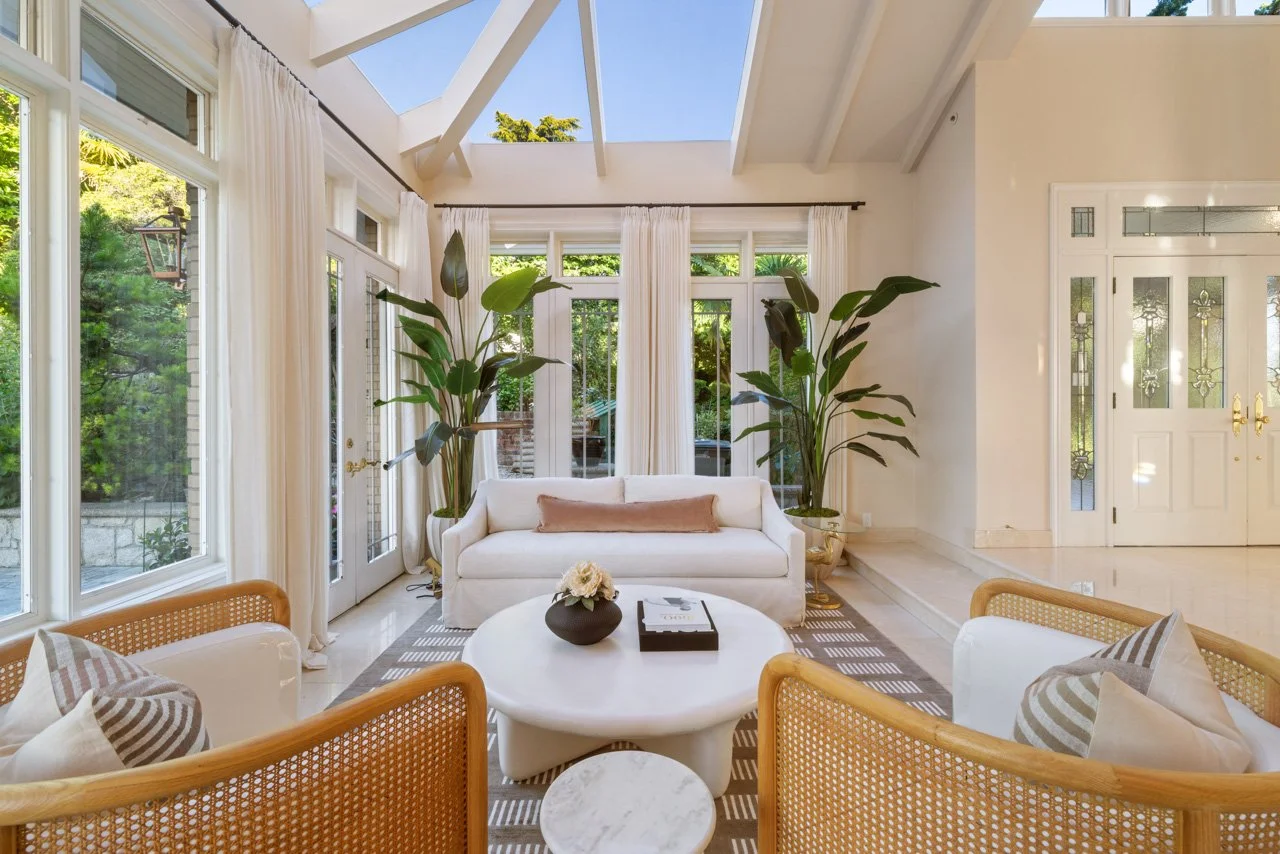 Sunny living room with white sofa, large windows, potted plants, and a skylight ceiling.