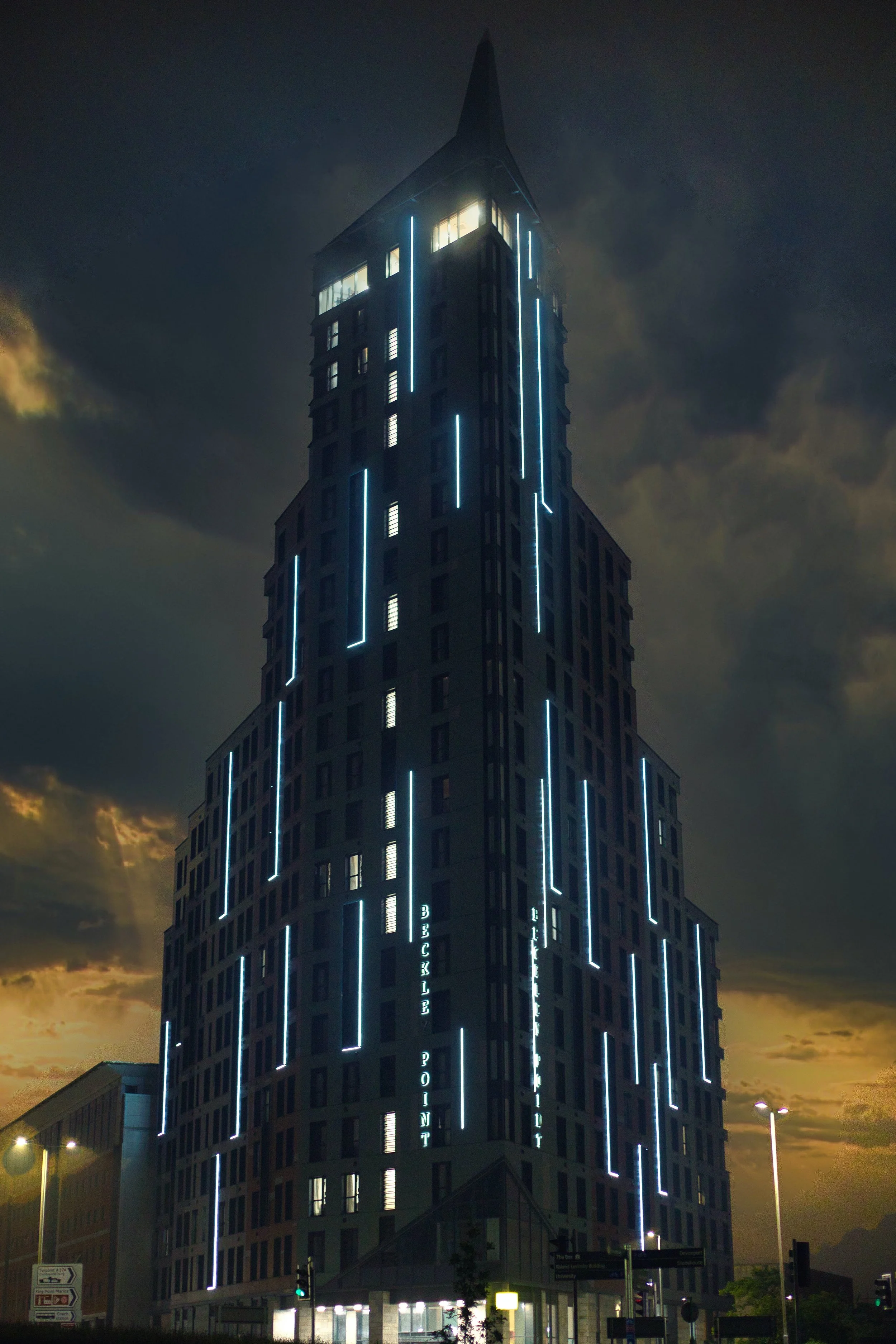 Nighttime photo of a tall modern building with illuminated vertical blue lines and the words "Buckley Point" on it.