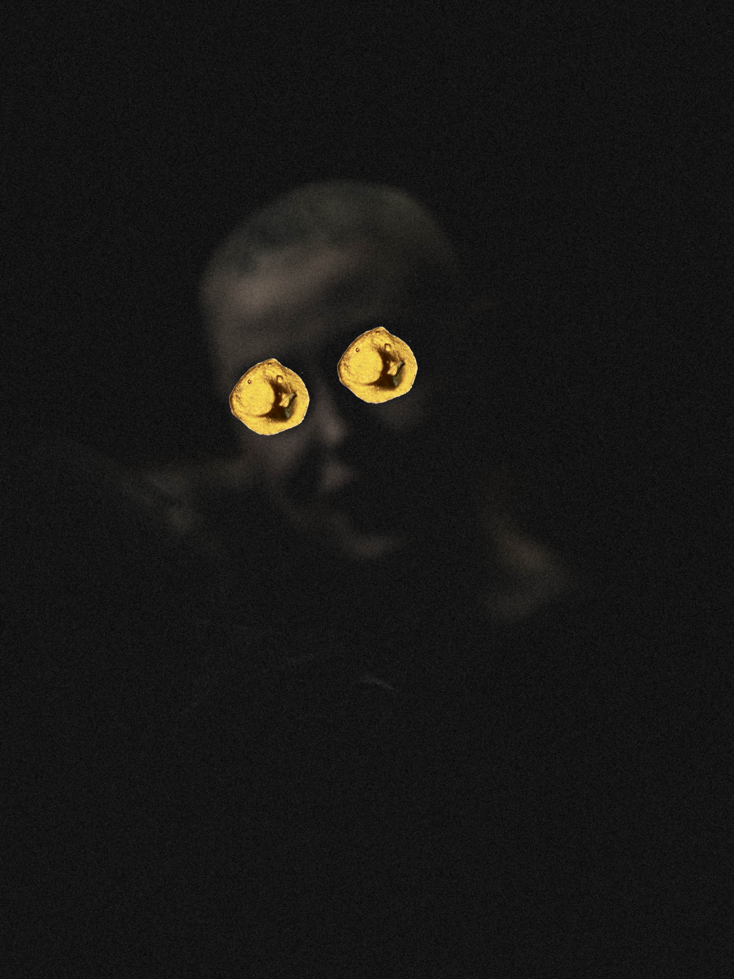 A dark image of a person's face with the eyes covered by yellow bananas.