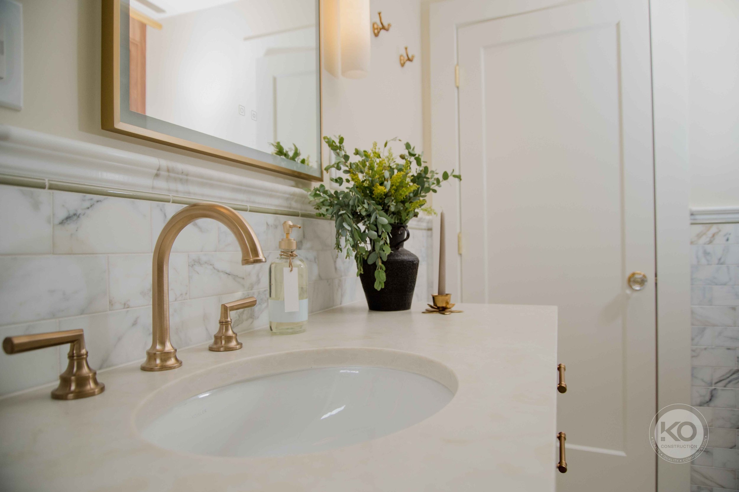 Quartz vanity countertop with warm brass faucet and marble wall detailing in a Federal Way bathroom remodel.