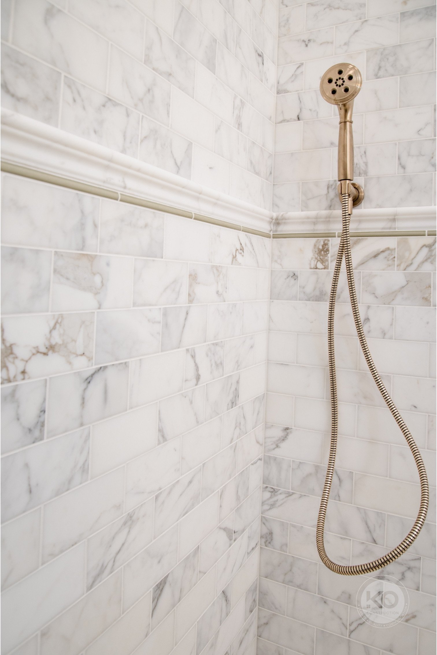 Brushed brass hand shower mounted on Calacatta Gold marble wall in a custom Federal Way bathroom remodel.
