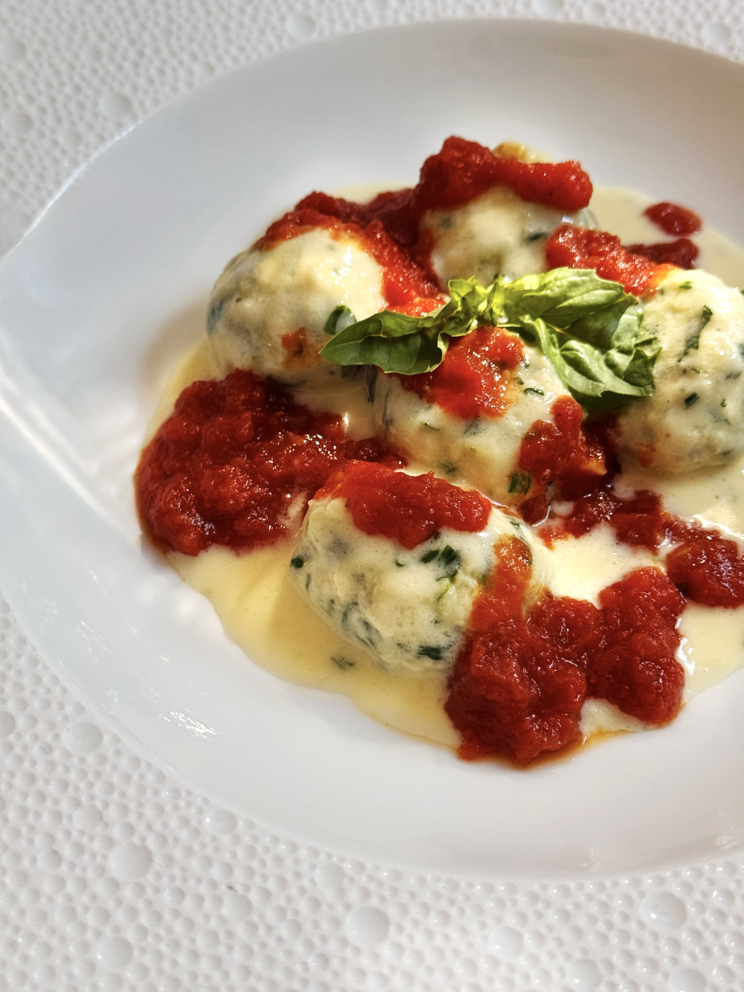 Ball of mozzarella cheese topped with tomato sauce and a basil leaf, served on a white plate.