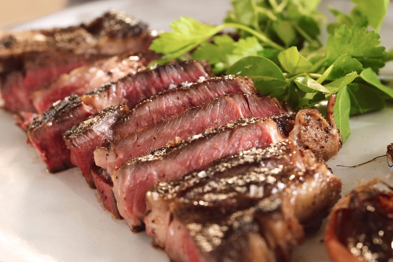 Slices of grilled steak with a green garnish on a white plate.