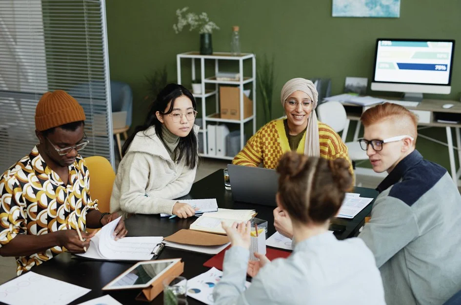 Group of people in discussion around table with computer and notes