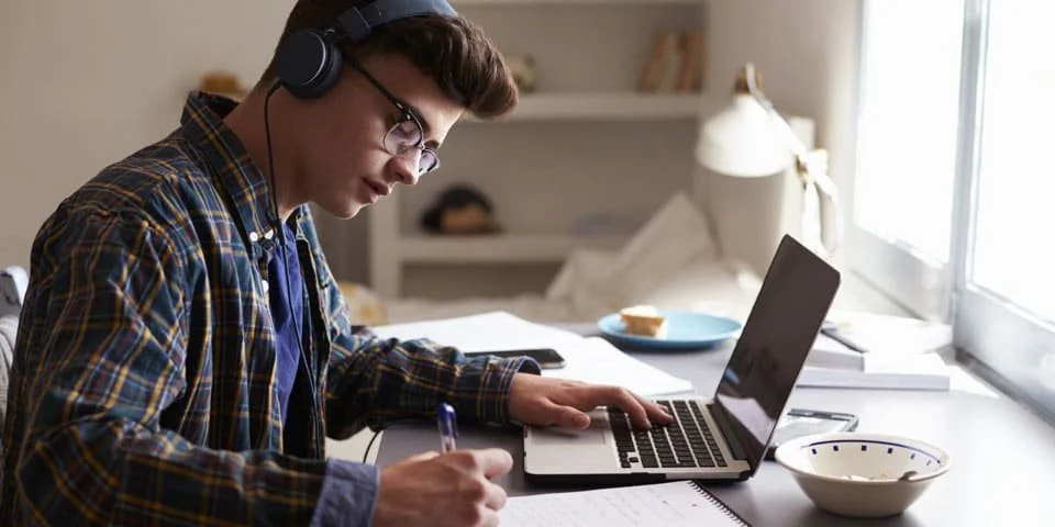 Person with glasses working at a computer with headphones.