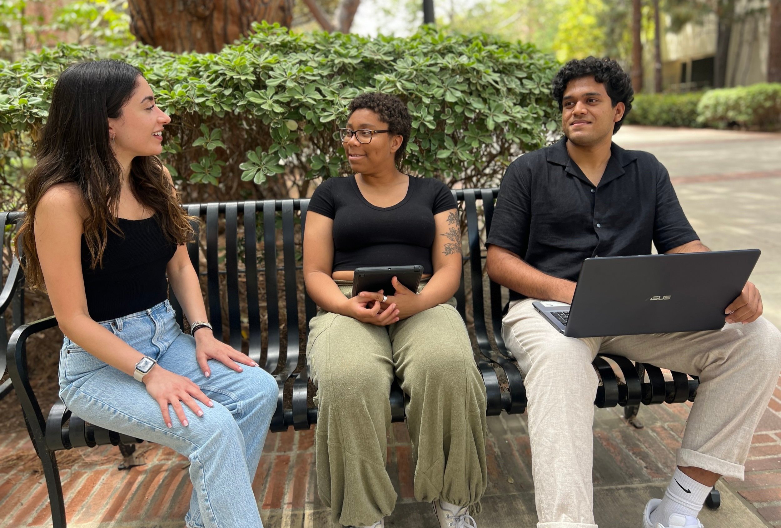 Three students sitting on a bench outside on UCLA's campus