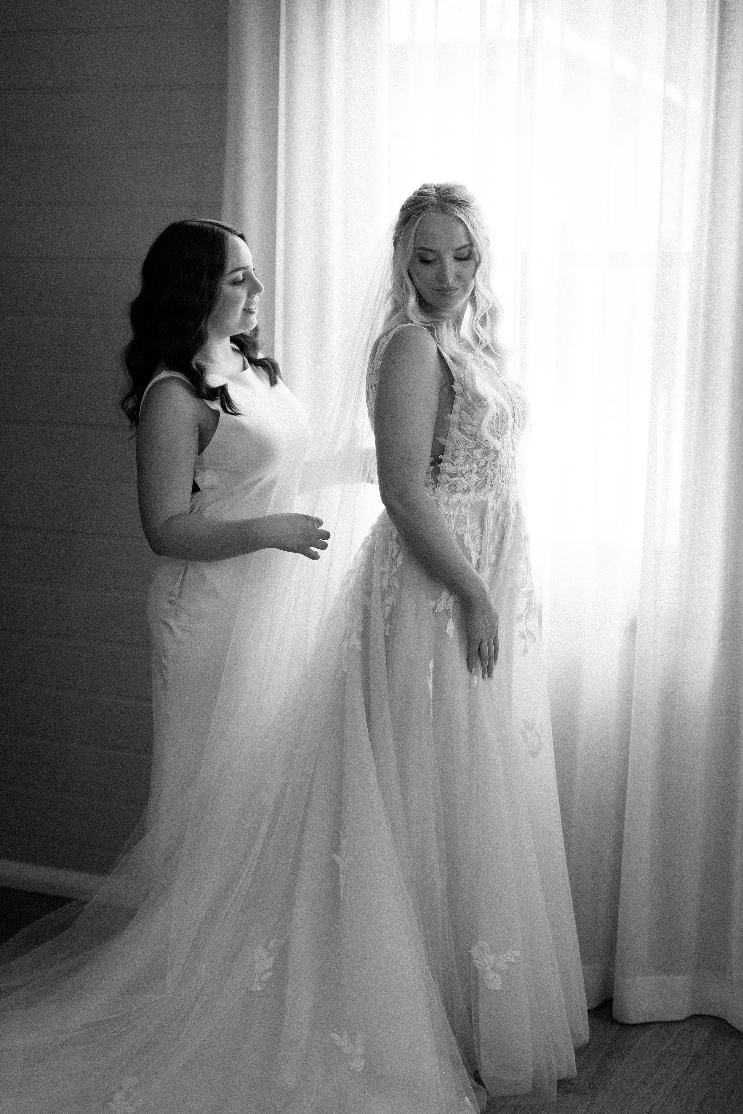 Two women preparing for a wedding, one in a wedding gown and the other adjusting her veil.