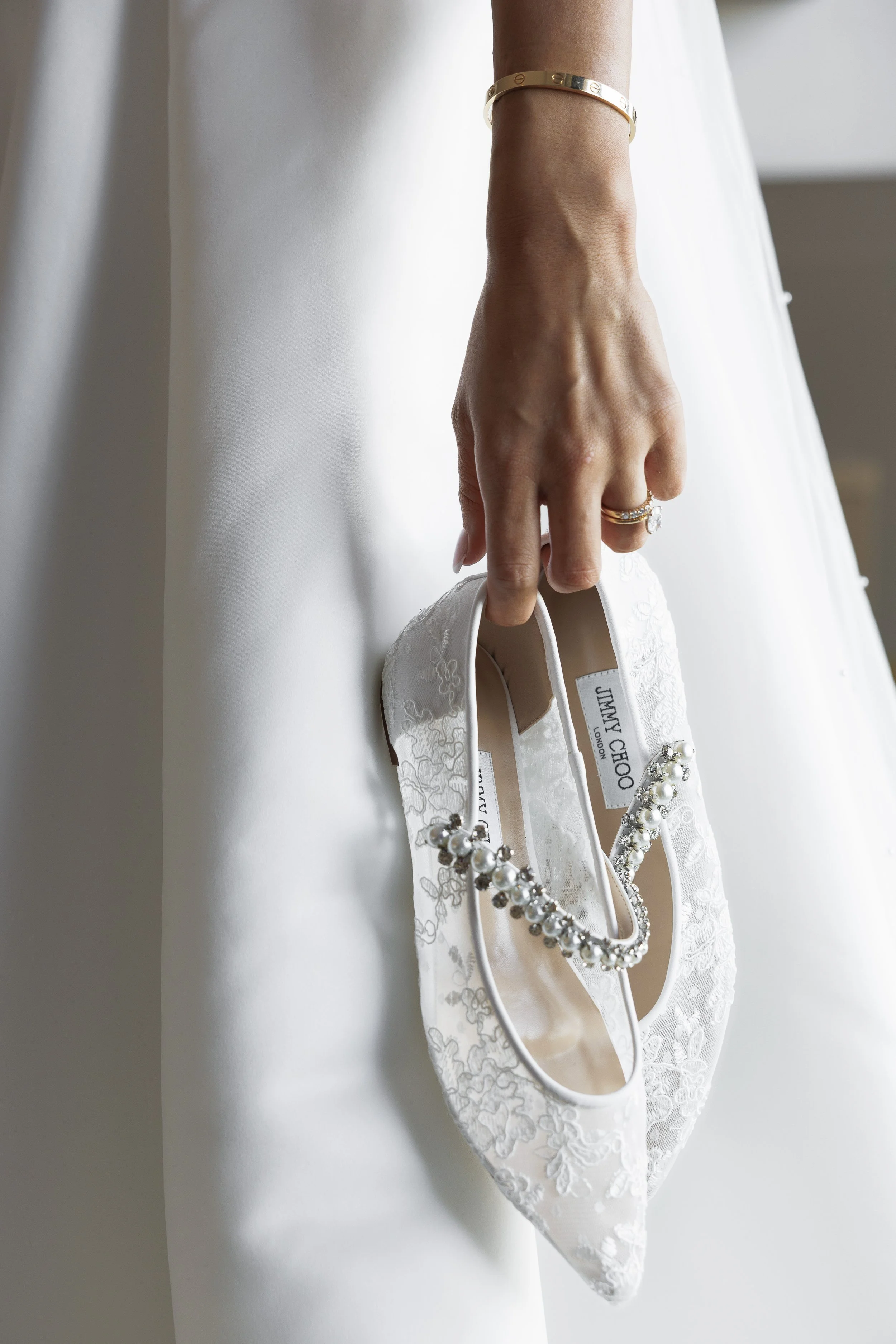 A woman in a white dress holds a white lace designer high heel shoe embellished with pearls and rhinestones.