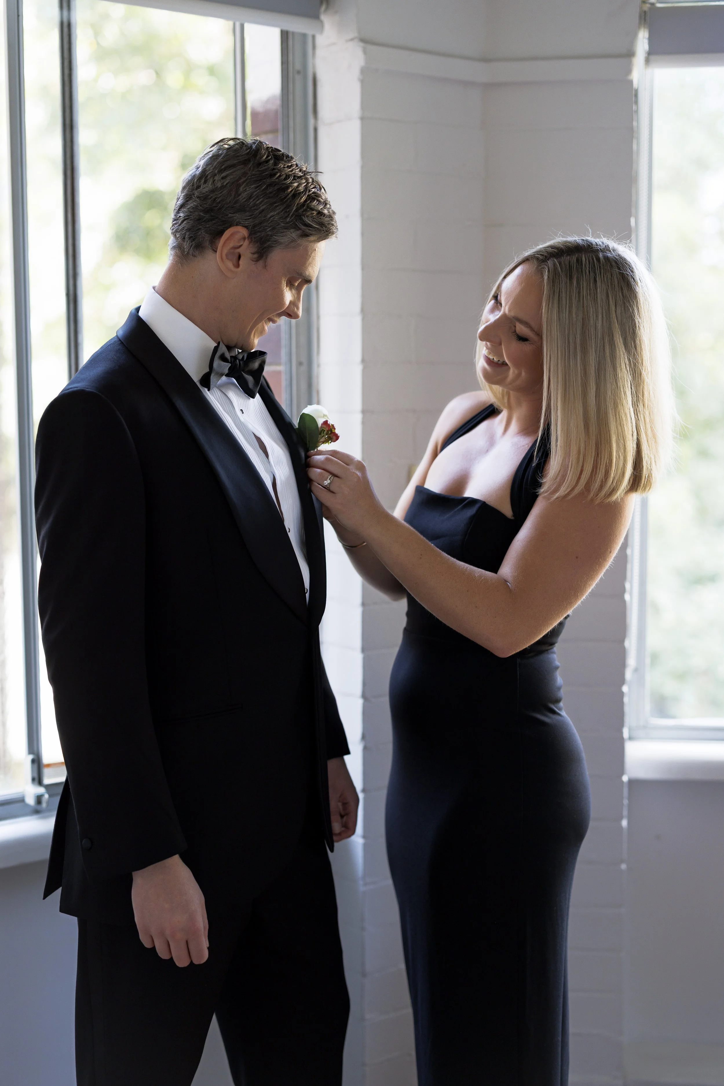 A woman is pinning a boutonniere on a man's tuxedo before a formal event or wedding.