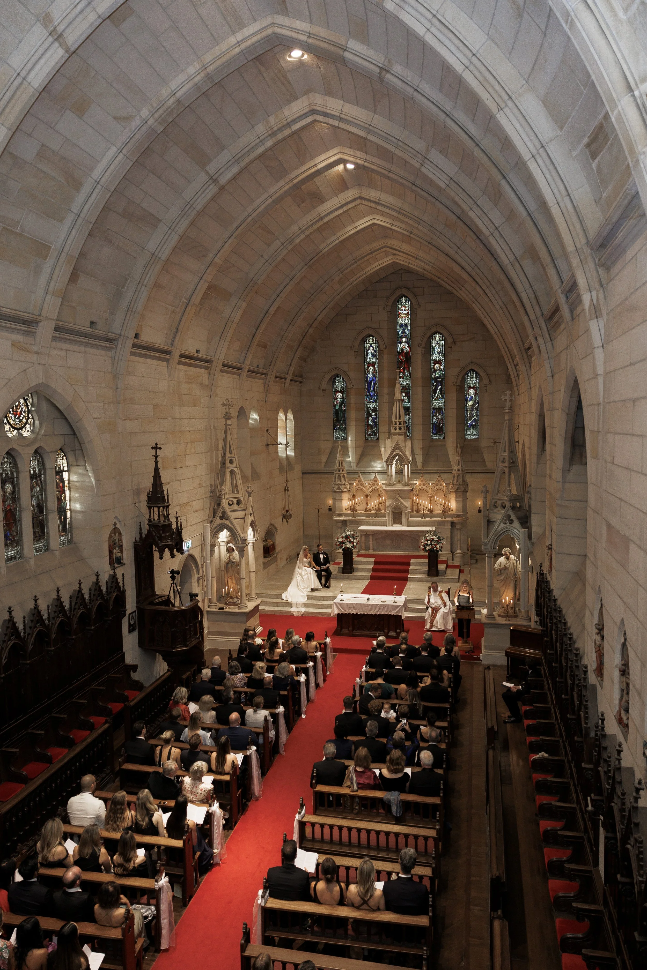 A wedding ceremony inside a church with an altar, stained glass windows, and pews filled with guests.