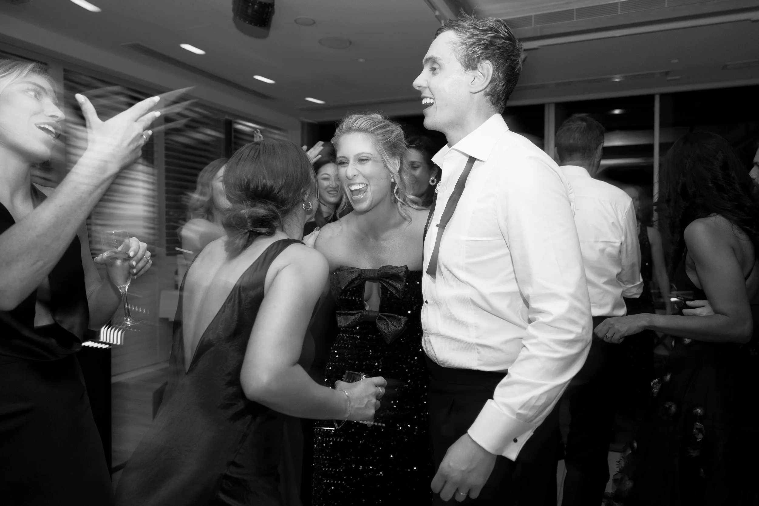 People at a party socializing and laughing, with some holding drinks, in a room with modern lighting.