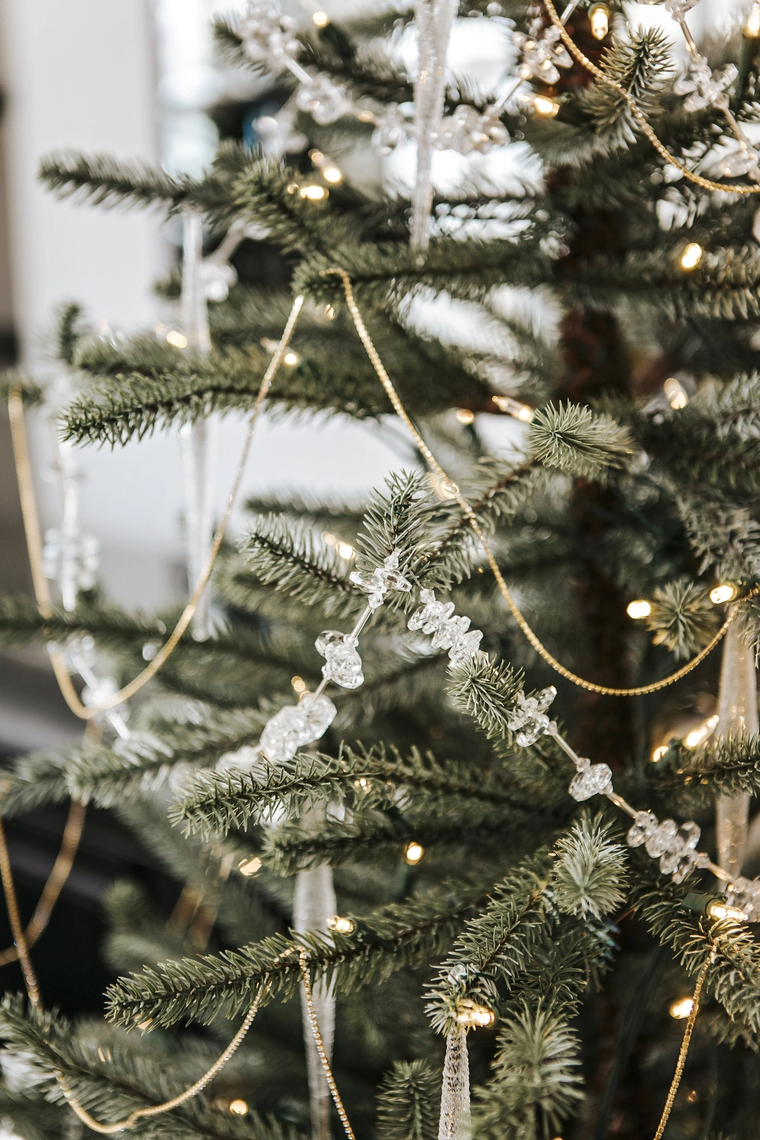 Close-up of a decorated Christmas tree with lights, gold beads, clear crystal ornaments, and white ribbon.