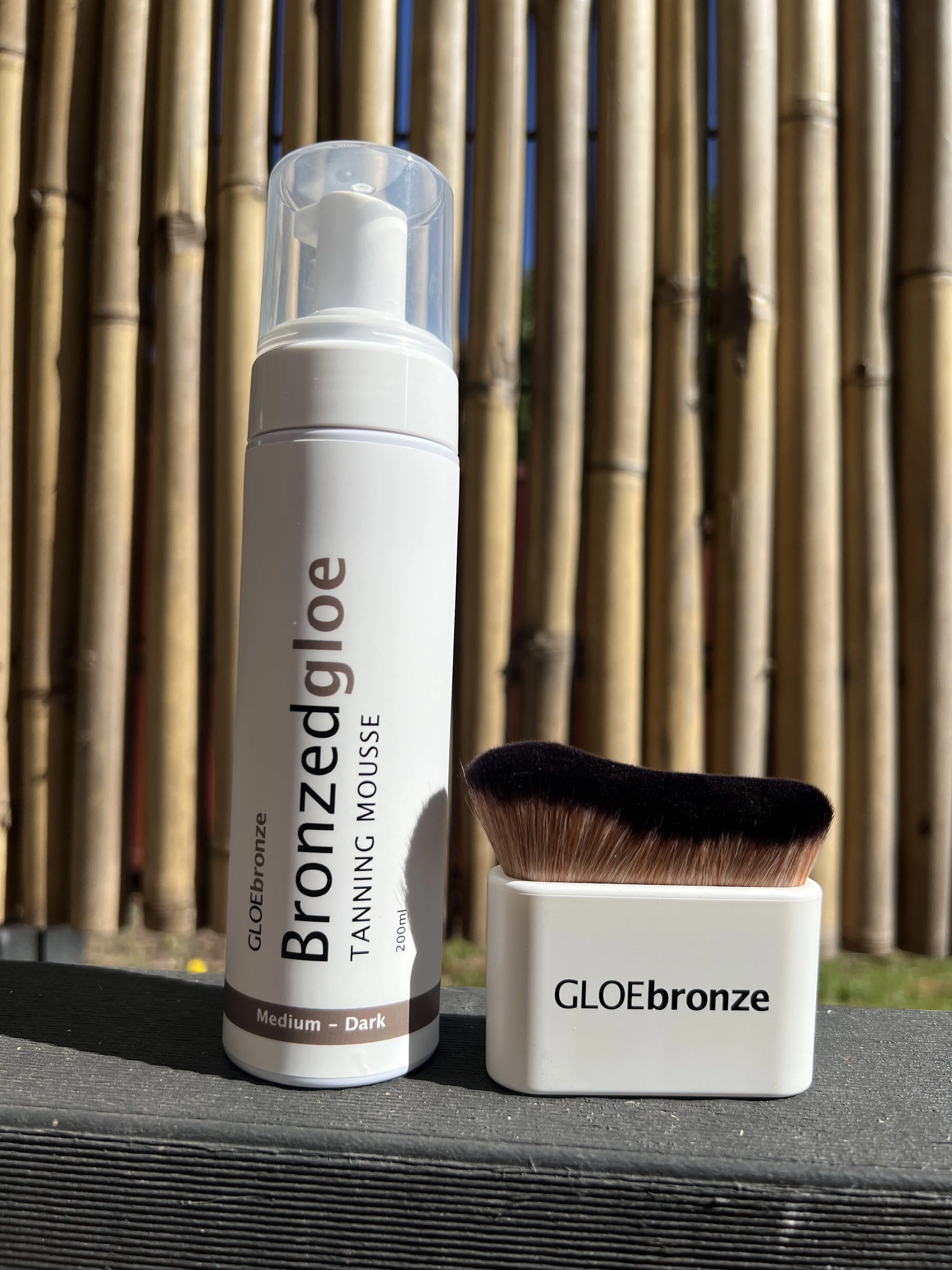 Bronzed GLOE bottle and tanning brush outdoors with natural light