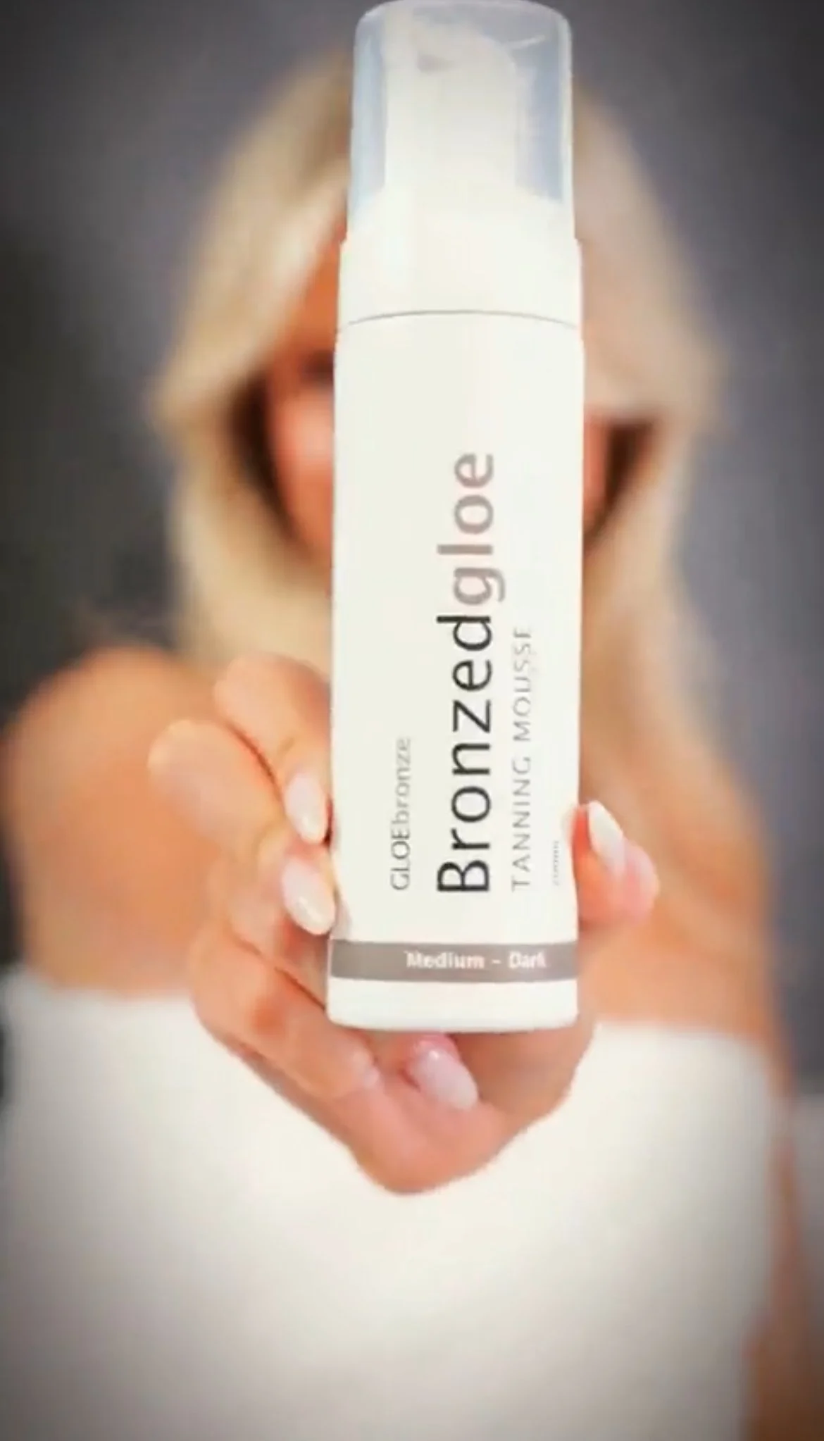 Model holding Bronzed GLOE Tanning Mousse bottle towards camera