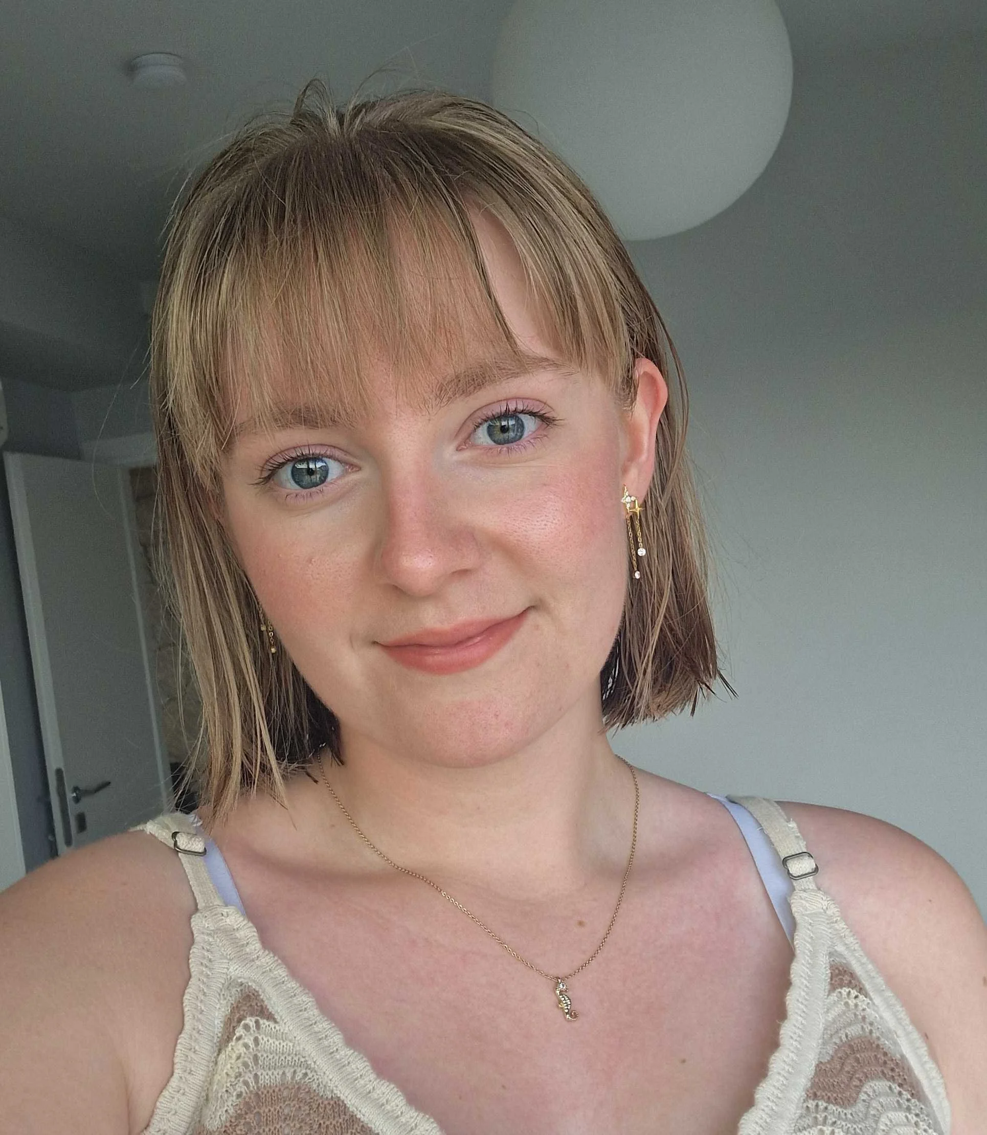 A young woman with shoulder-length brown hair leaning against a concrete wall outdoors, smiling at the camera.