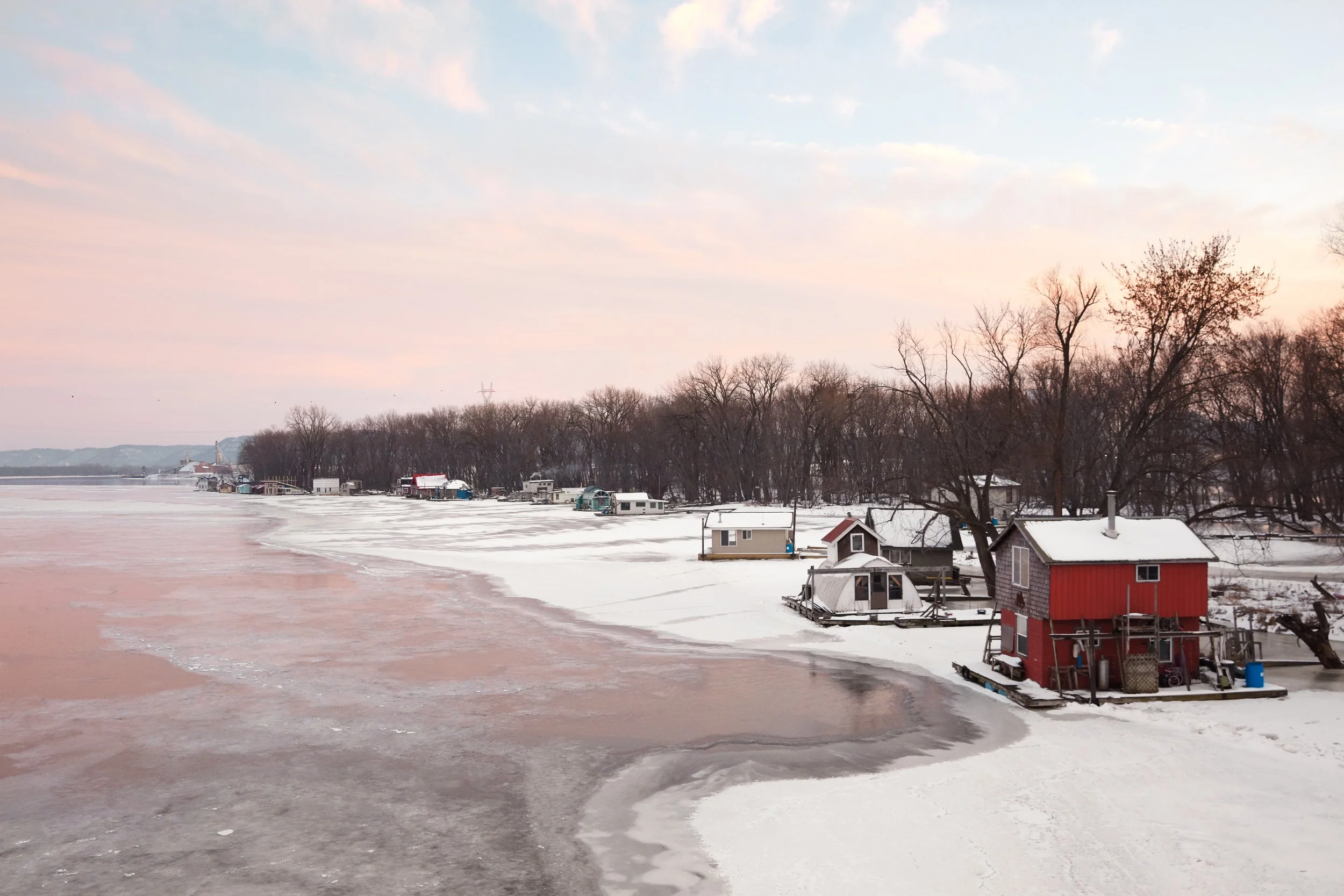 Le soleil se lève sur de petites maisons situées au bord d’un lac gelé