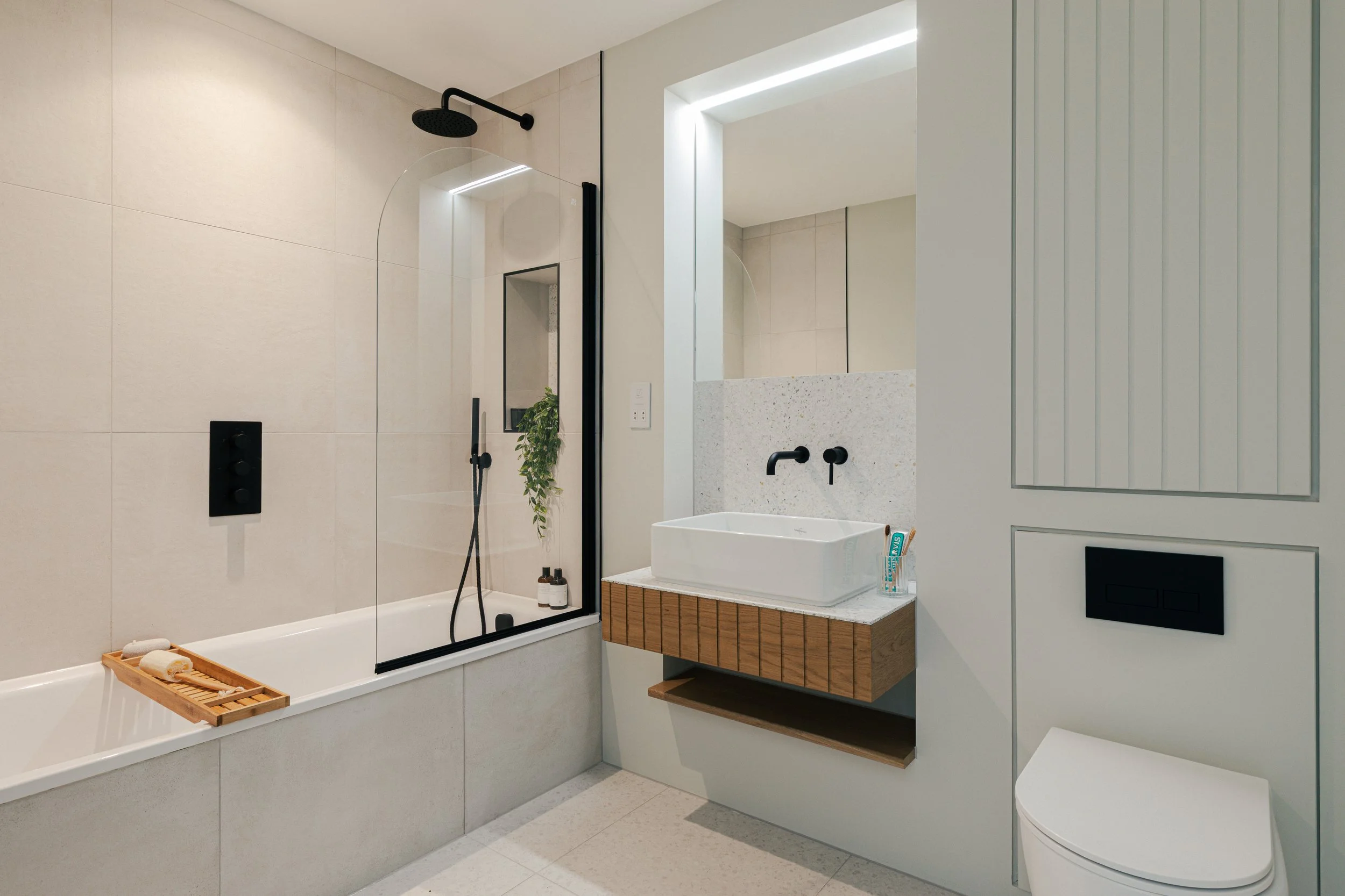 Modern bathroom with bathtub, glass shower enclosure, wall-mounted sink, large mirror, and minimalist decor.