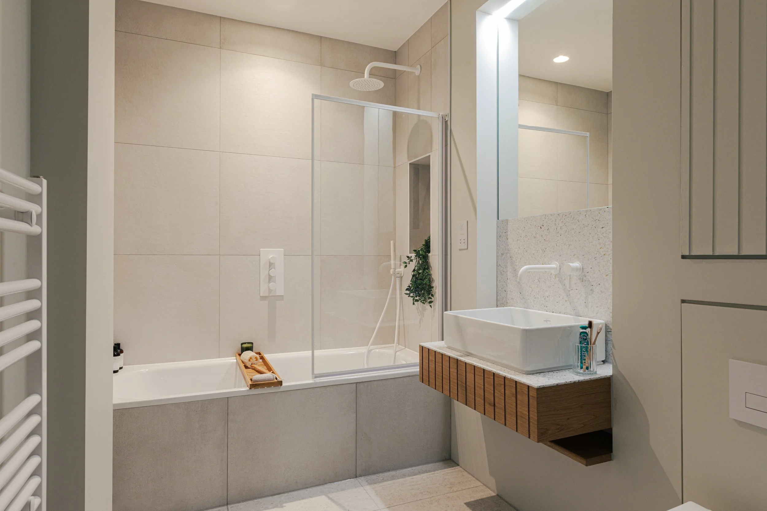 Modern bathroom with a bathtub, shower with a glass barrier, a white rectangular sink on a wooden vanity, and a mirror.