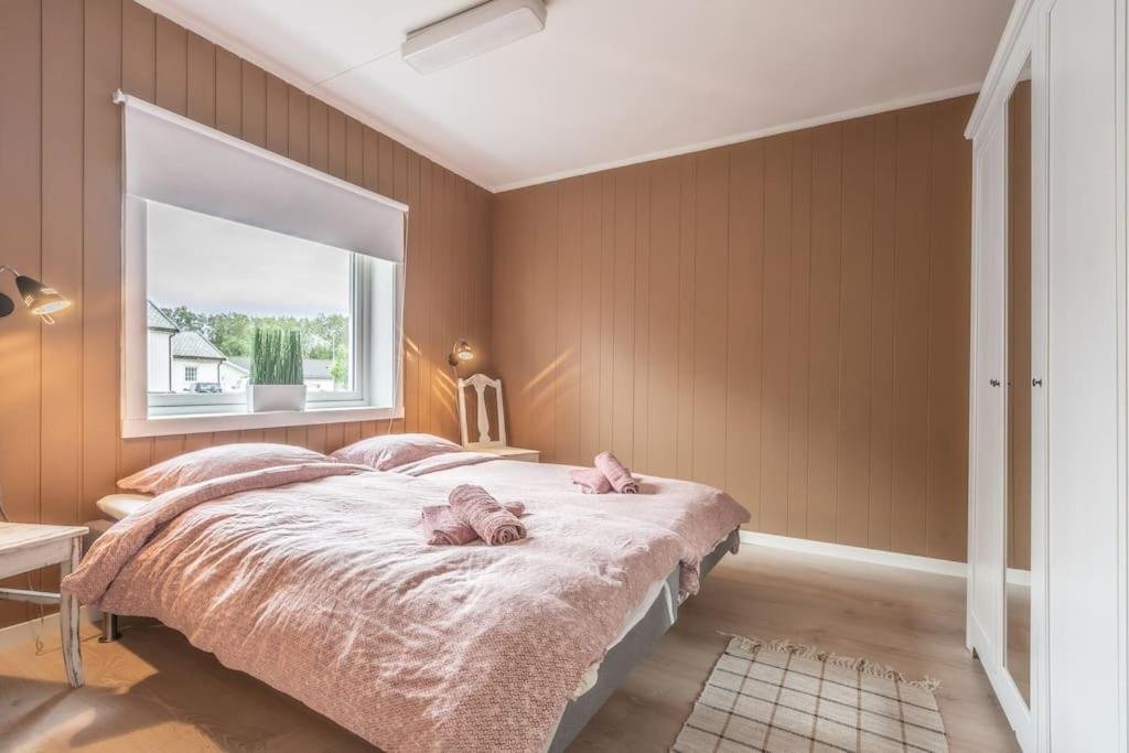 Cozy bedroom with a double bed, pink bedding, and brown paneled walls. A window with a view and a white wardrobe are present.