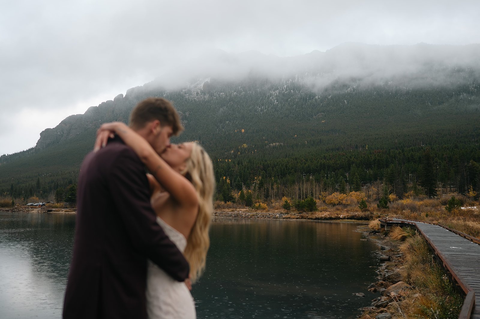a bride and groom embracing with the gloomy mountain view and lake behind them