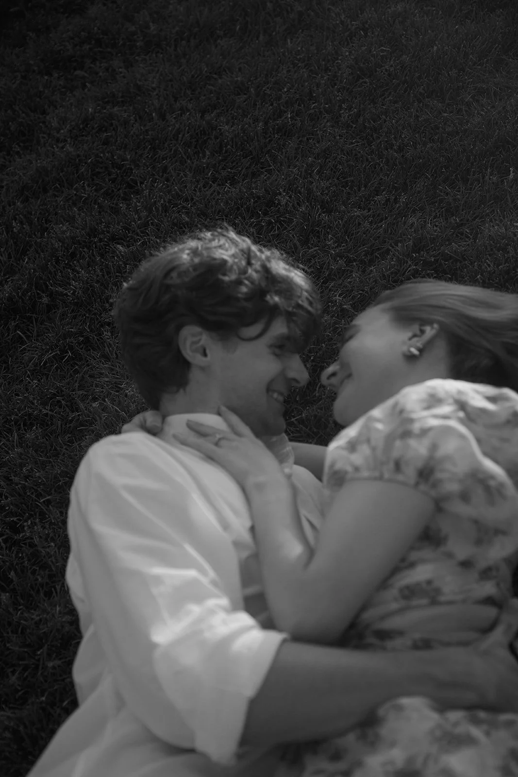 a candid engagement photo of a couple laying in the grass an laughing