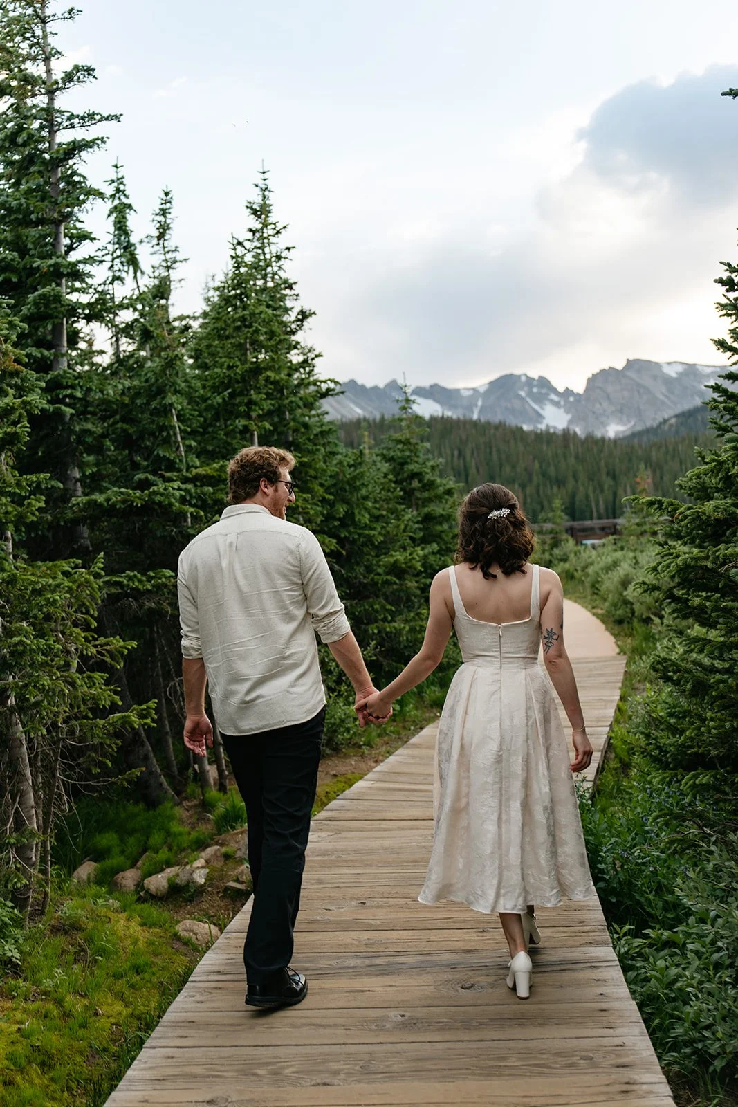 a couple walking towards the mountains on a trail through the trees at a Engagement Photo Location in Colorado