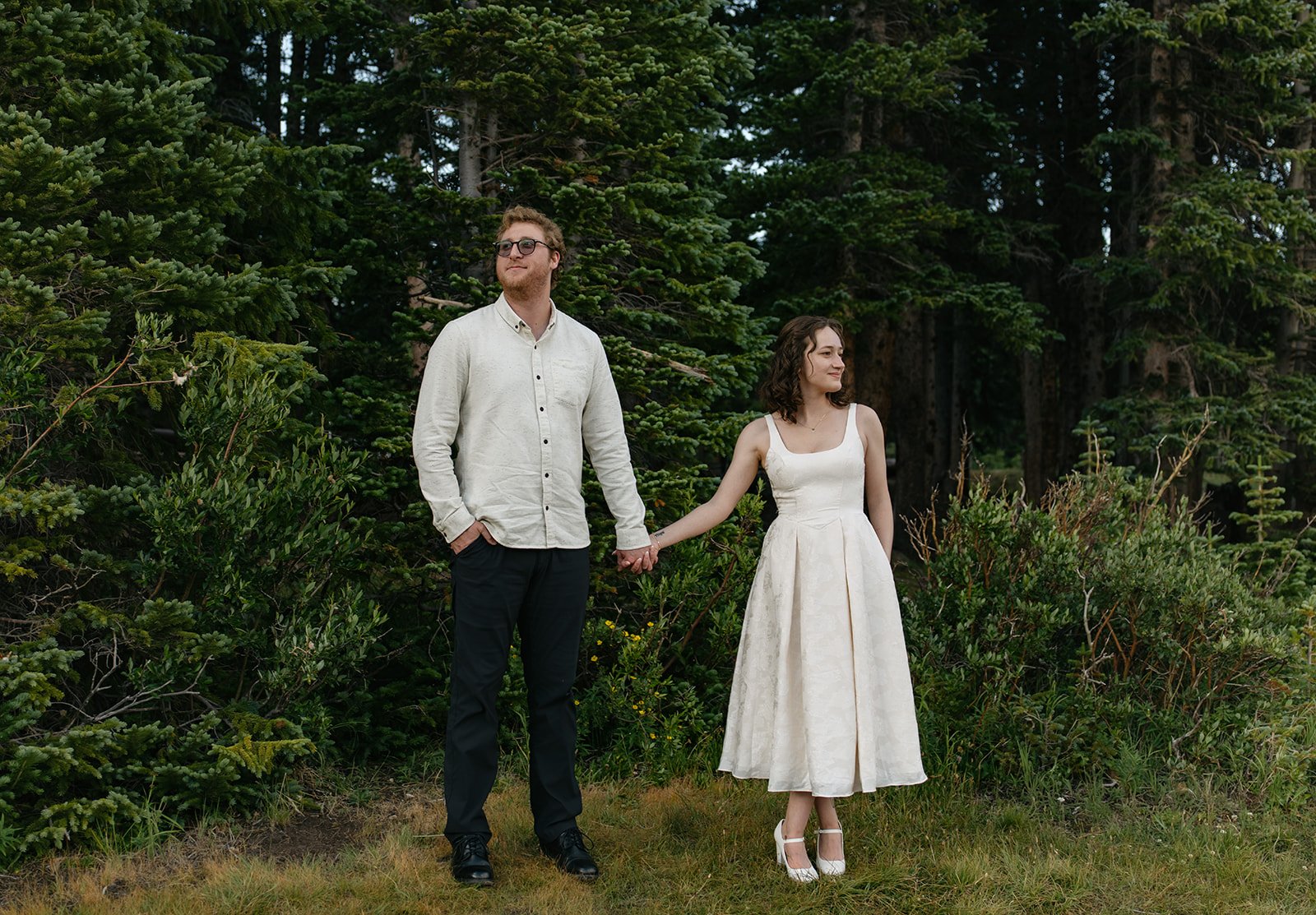 a couple holding hands in front of evergreen trees in Colorado for engagement photos