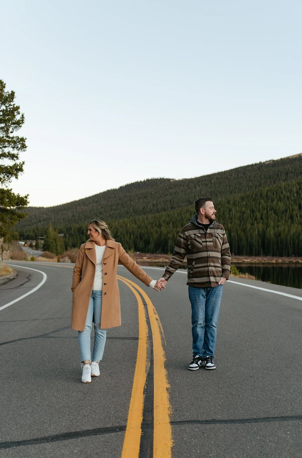 newly engaged couple walking hand in hand on a road with the mountains behind them for engagement photos