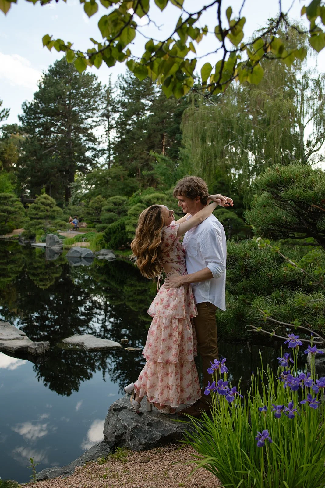 a couple holding each other by a pond in a garden for their engagement photos