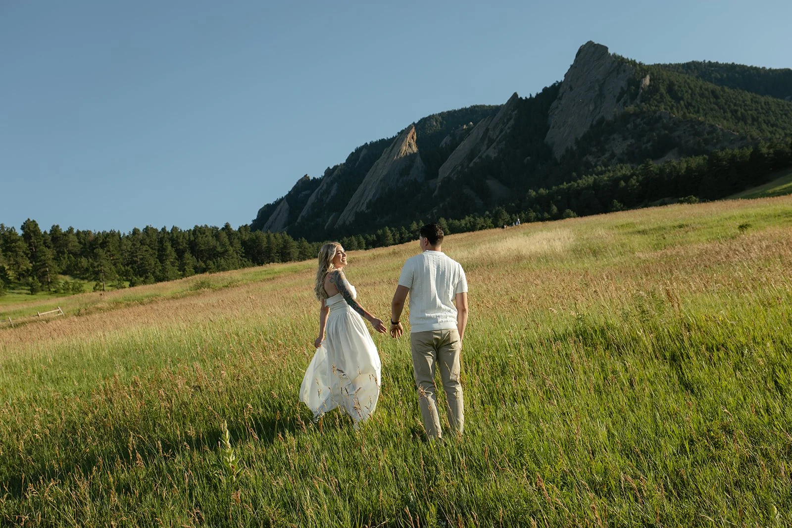 a couple walking through a grass field together for engagement photos in CO