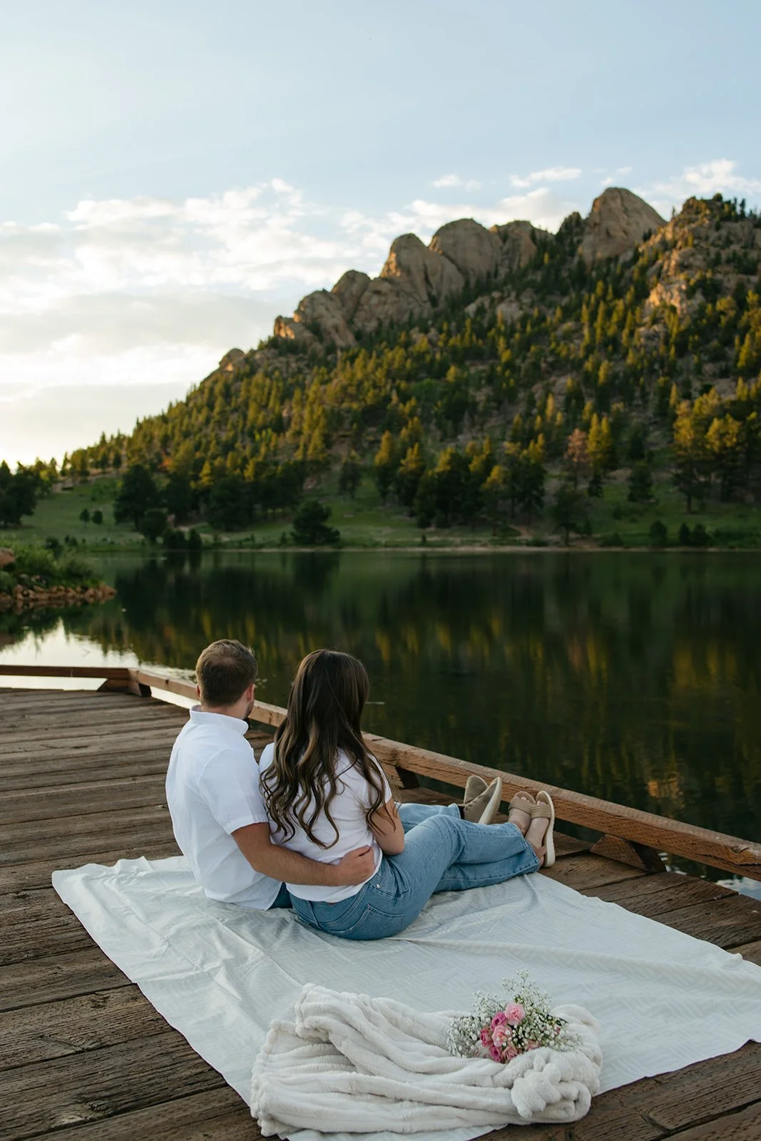 a couple sitting on a dock looking out at the lake and mountains at a favorite Engagement Photo Location in Colorado