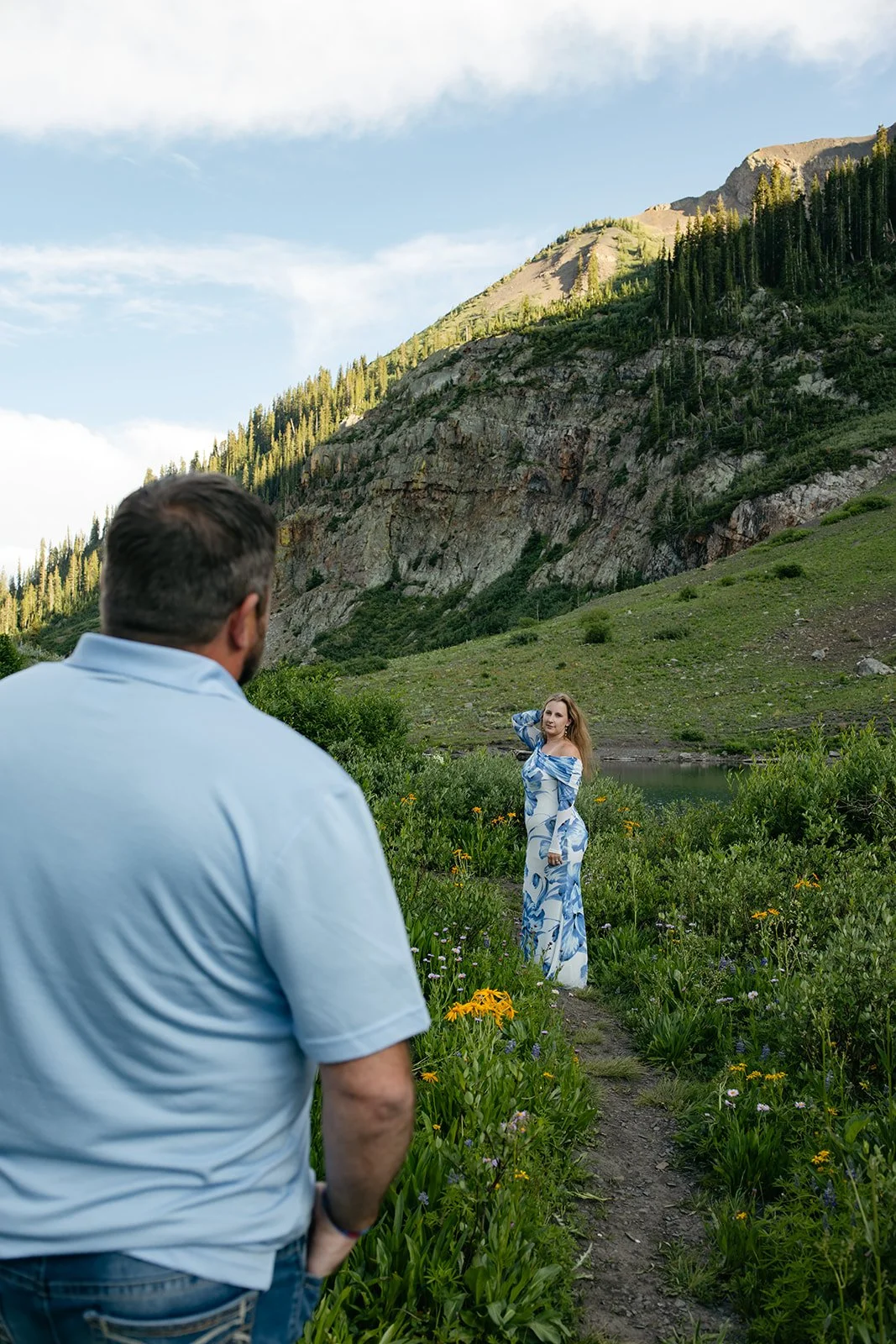 a man watching a woman pose on a trail with wildflowers at a Colorado Engagement Photo Location
