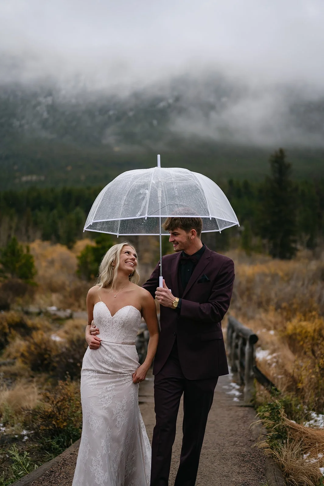a couple smiling as they walk under an umbrella during their elopement photos in CO