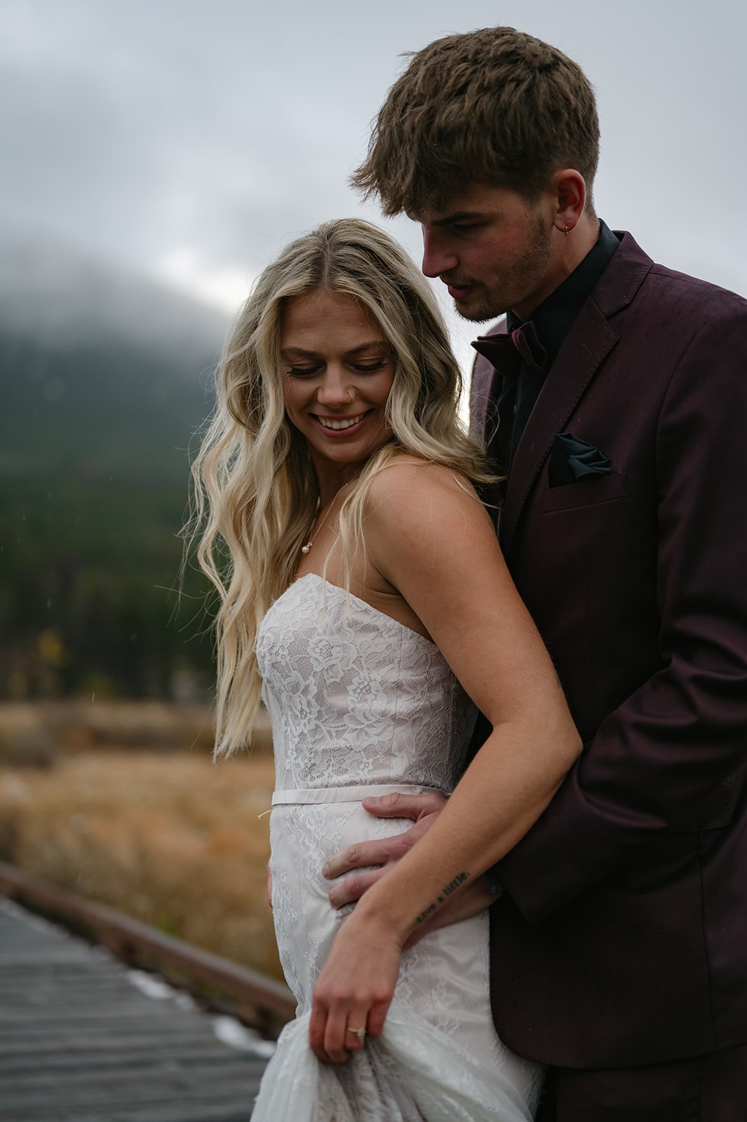 a man holding his bride from behind as they dance in the mountains