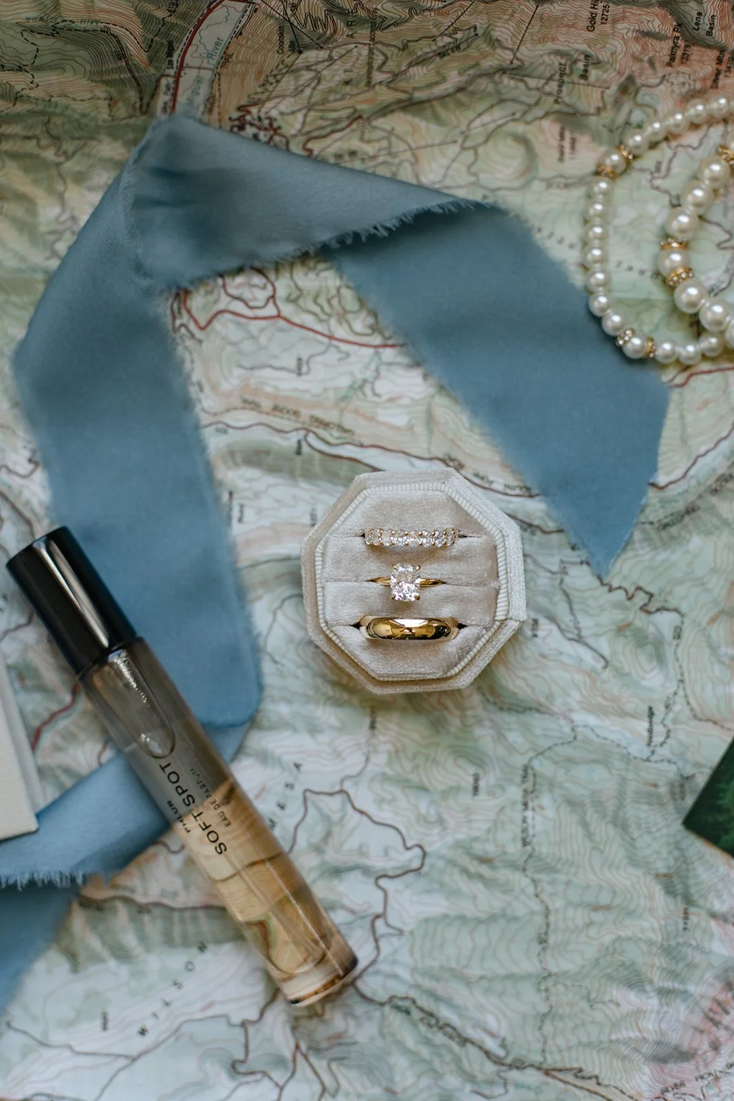 a ring box, a ribbon and perfume laid out on a map for Wedding Detail Photos