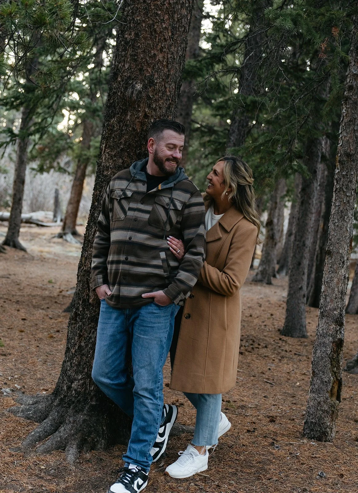 newly engaged couple standing in the woods for their engagement photos