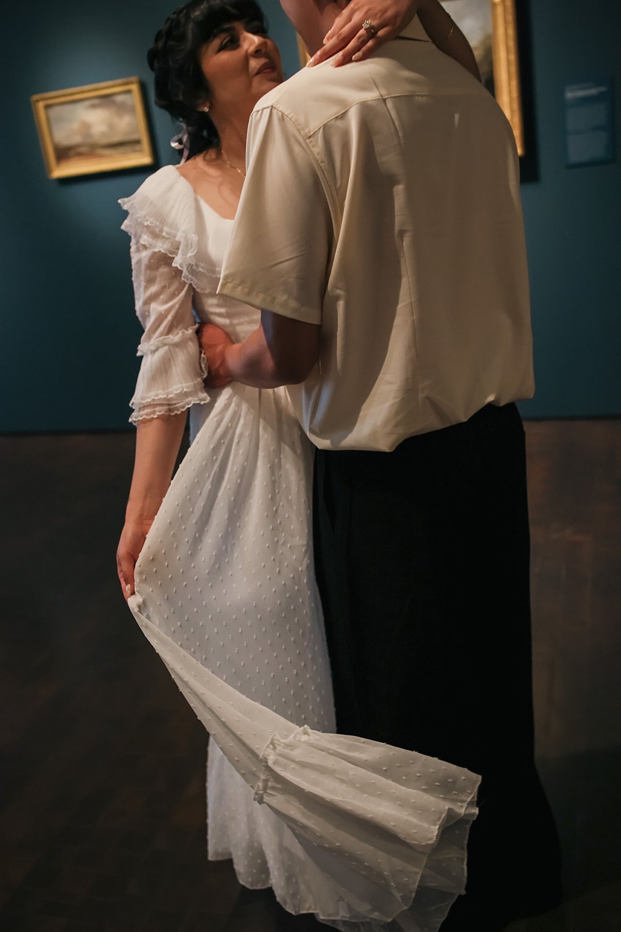 A tender candid of a couple dancing closely inside a museum, with flowing fabric and artwork in the background adding warmth and texture.