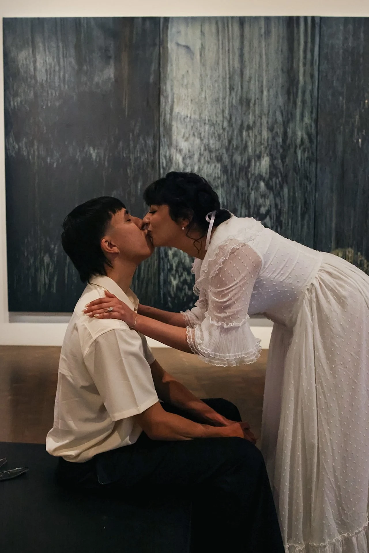 A playful moment of a couple sharing a kiss in front of a large abstract painting, blending modern art with timeless romance.