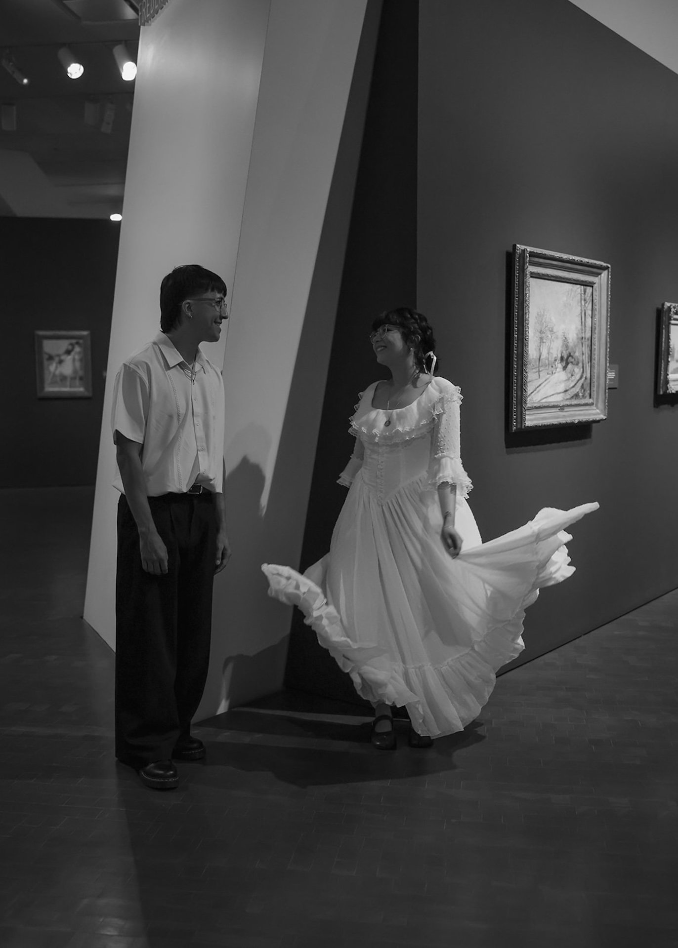 A candid black and white moment of a couple laughing together between gallery walls, showcasing relaxed, documentary-style city engagement photos in an art-filled space.