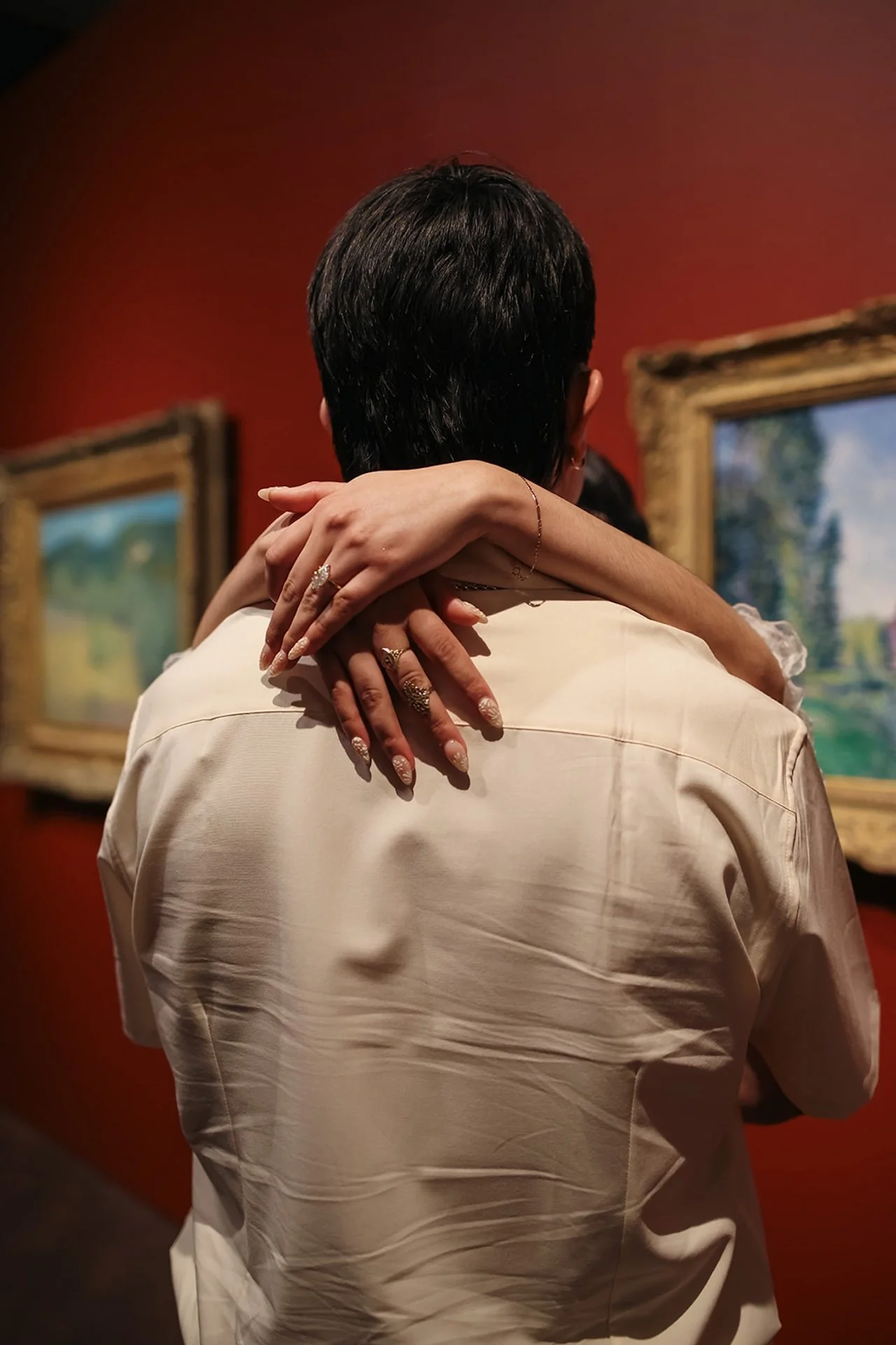 A close, intimate moment of a couple embracing inside an art museum, with soft lighting, warm red walls, and framed paintings creating a romantic city engagement photos vibe.