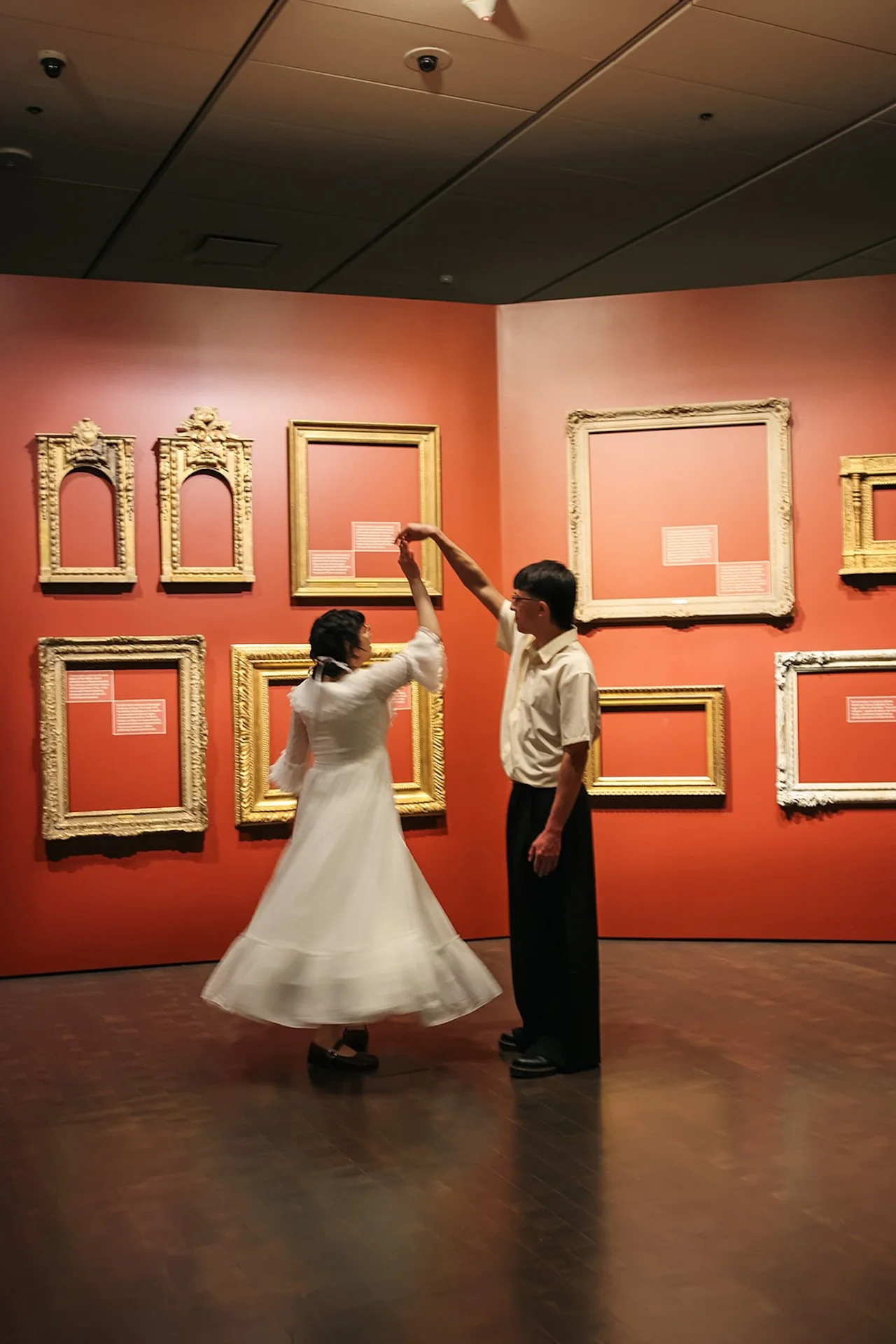 A playful moment of a couple twirling together inside a museum gallery filled with empty gilded frames, creating artistic and creative city engagement photos.