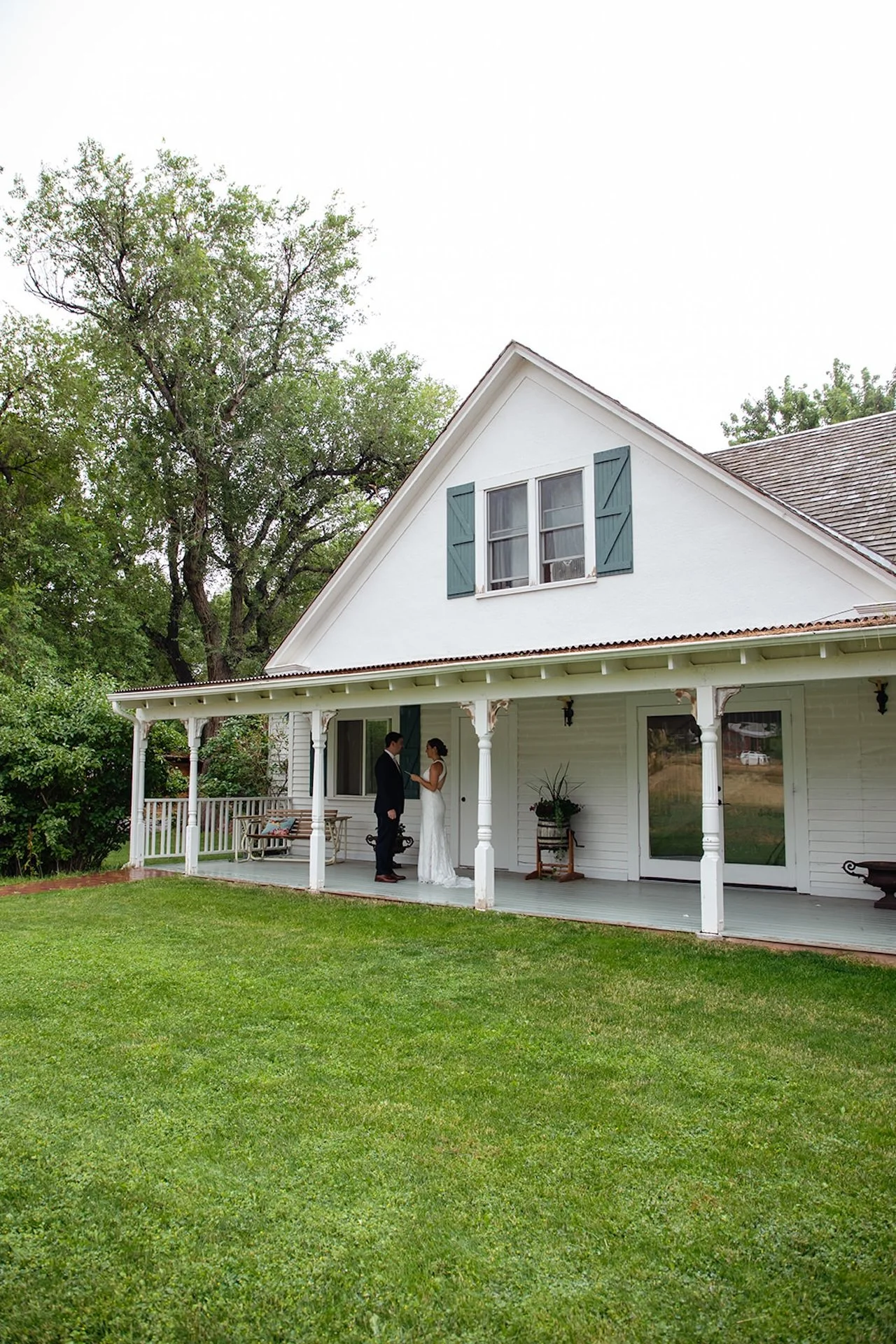 Bride and groom sharing an intimate moment on the porch of a charming white farmhouse at their Fort Collins Wedding Venue.