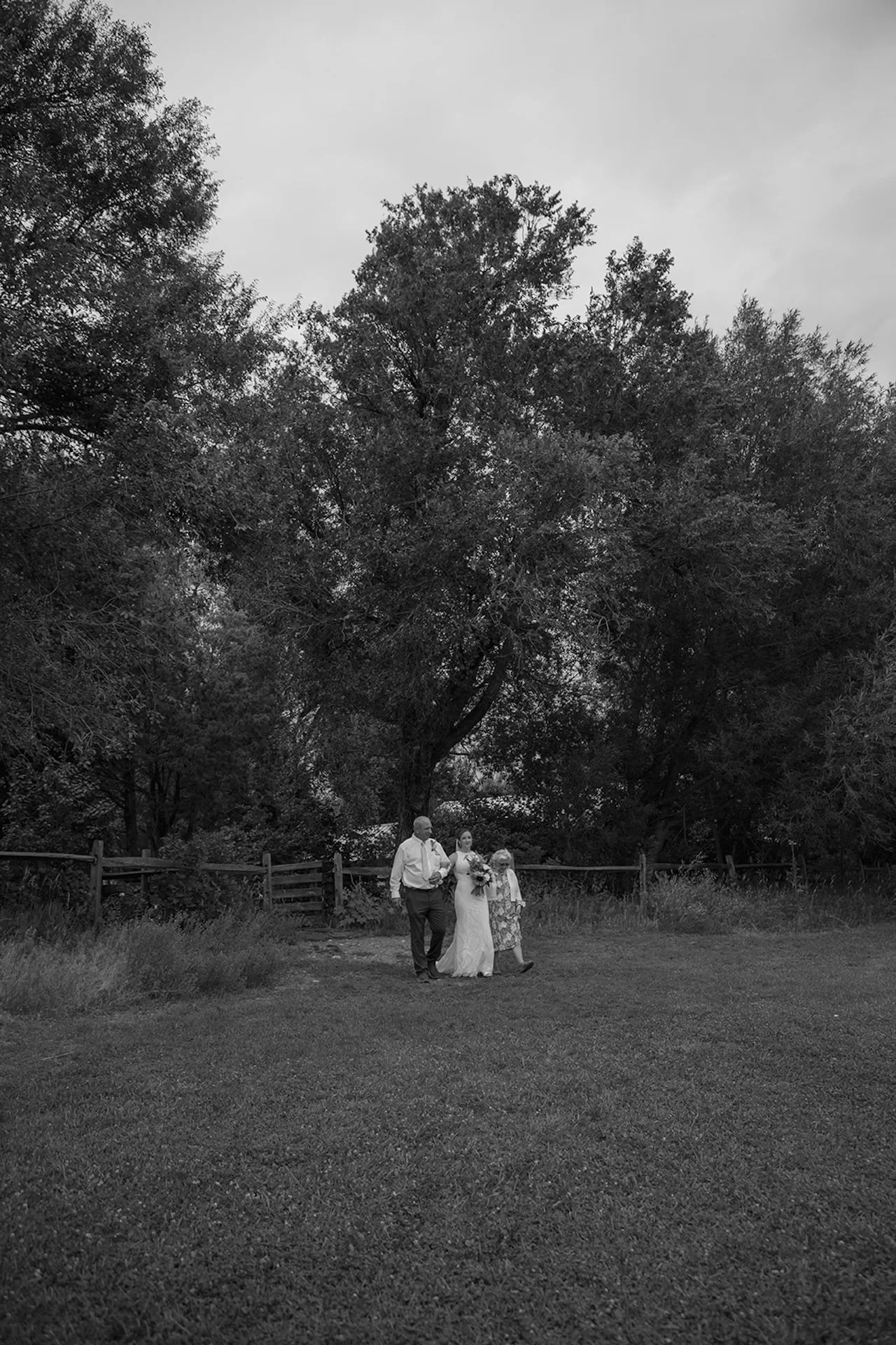 Bride walking across the lawn with her parents in a black and white candid moment before the outdoor wedding ceremony.