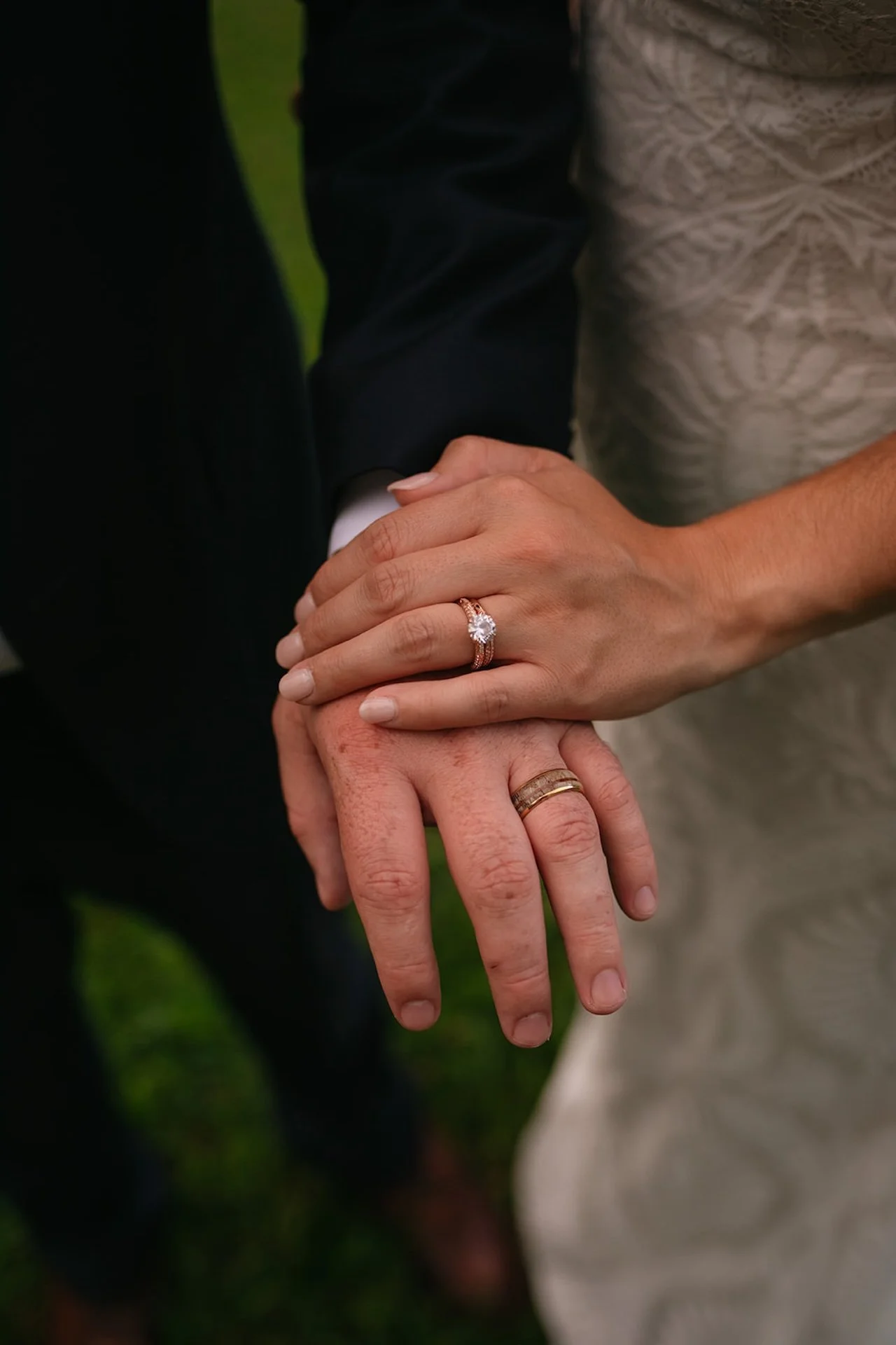 Close-up of the bride’s engagement ring and wedding band resting on the groom’s hand during an outdoor wedding portrait.