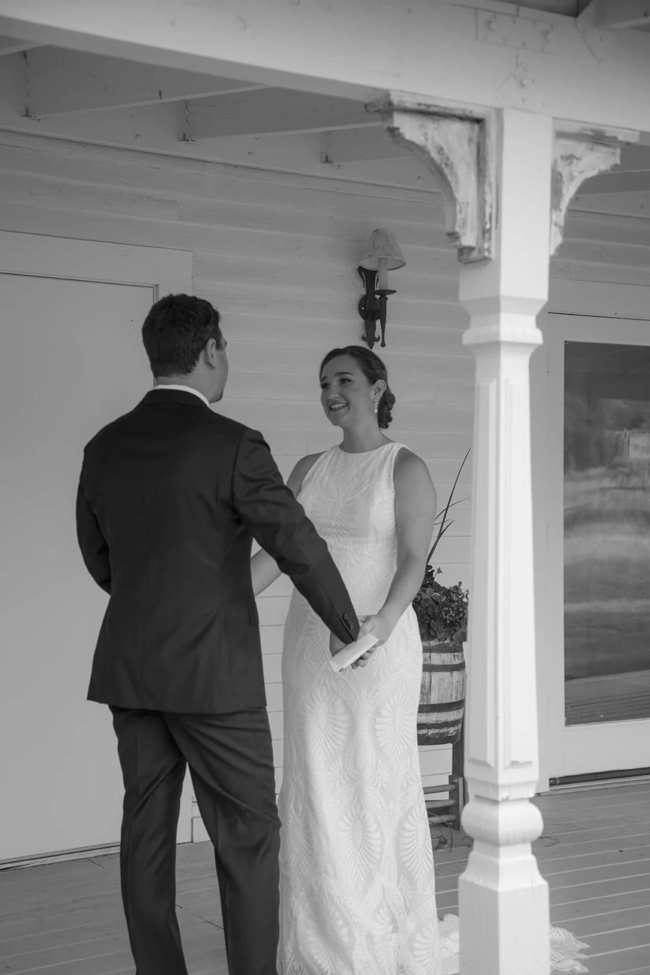 A black and white photo of the bride and groom holding hands on a white porch during their first look.